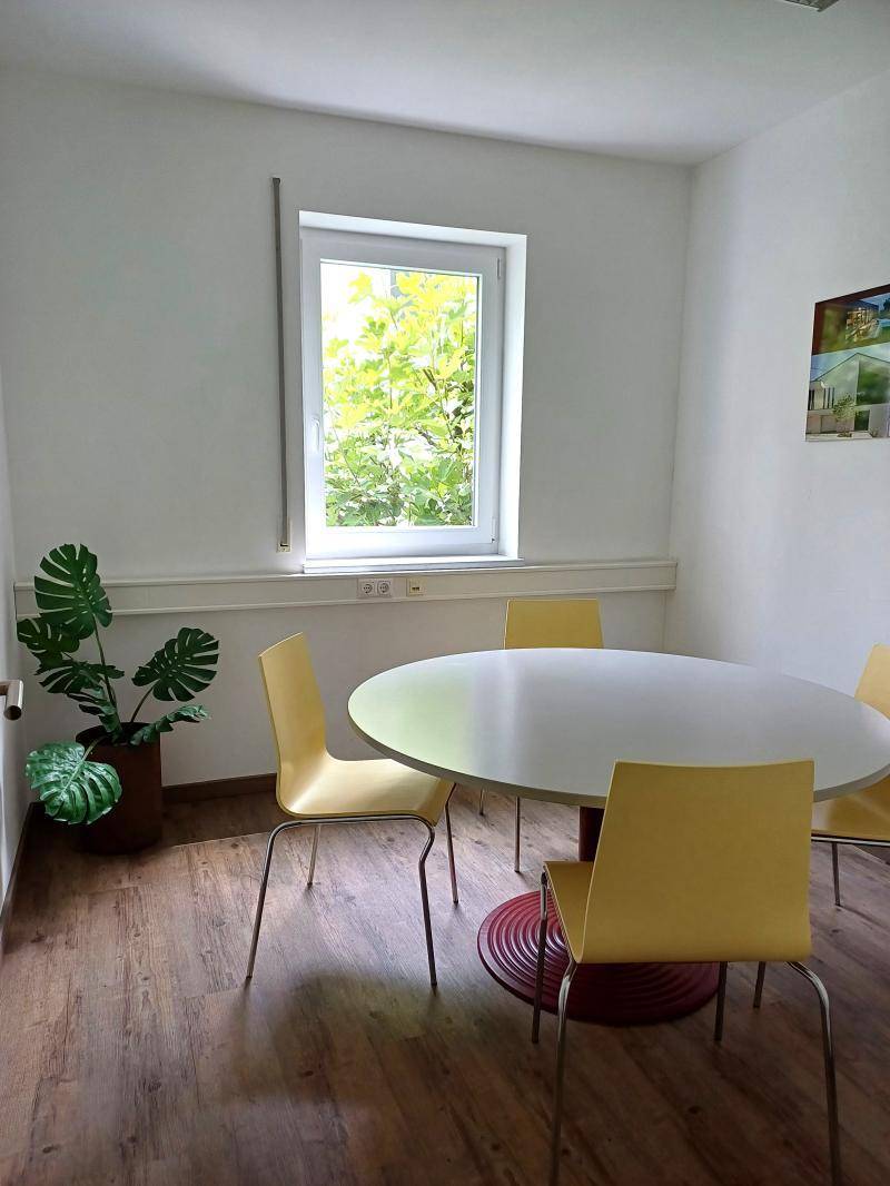 Besprechungsraum mit rundem Tisch, gelben Stühlen und einem Fenster mit Blick ins Grüne.