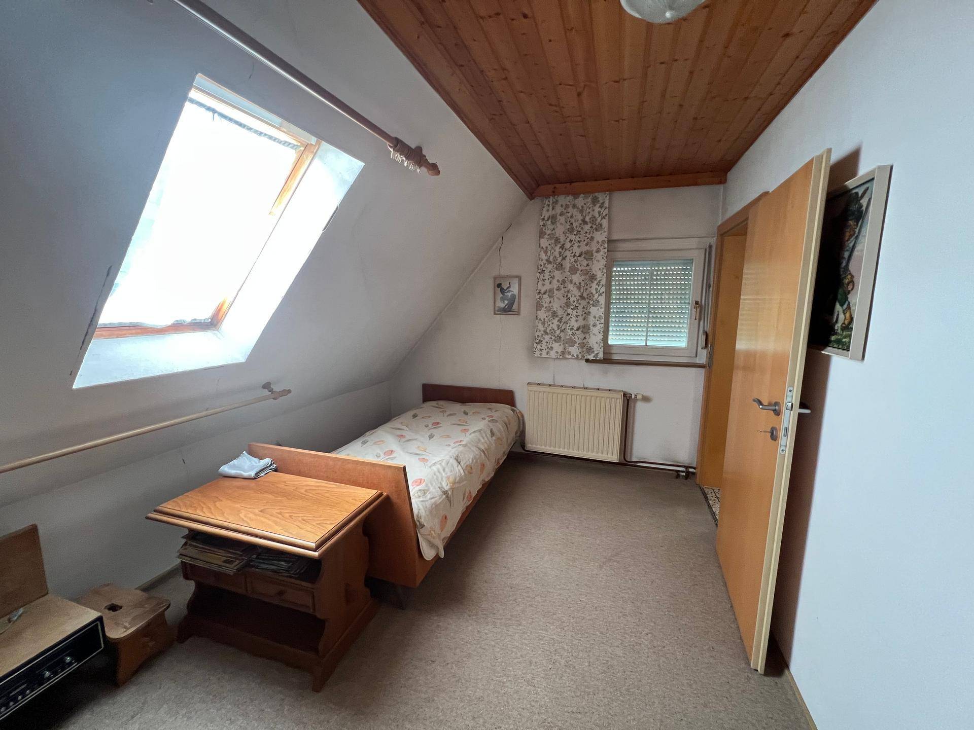 Kleines Dachzimmer mit Einzelbett, Holzdecke und Dachfenster für natürliches Licht.