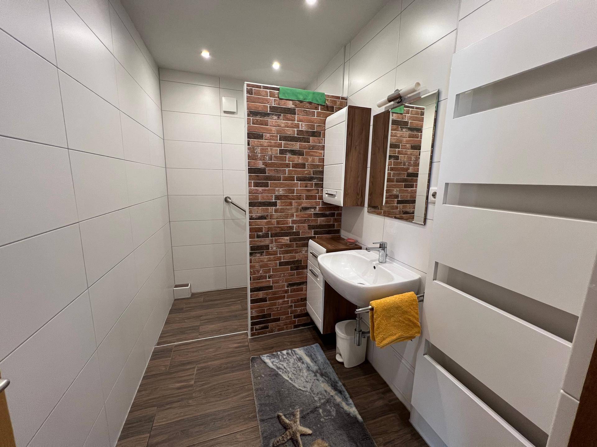Modernes Badezimmer mit weißen Fliesen, Ziegelwandakzent und barrierefreier Dusche.