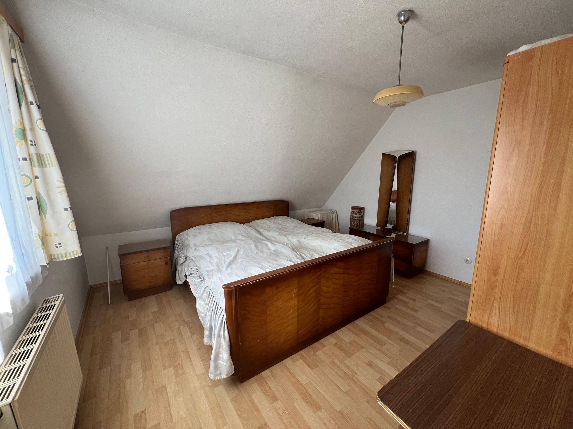 Dachgeschoss-Schlafzimmer mit Holzbett, Laminatboden und schräger Decke.