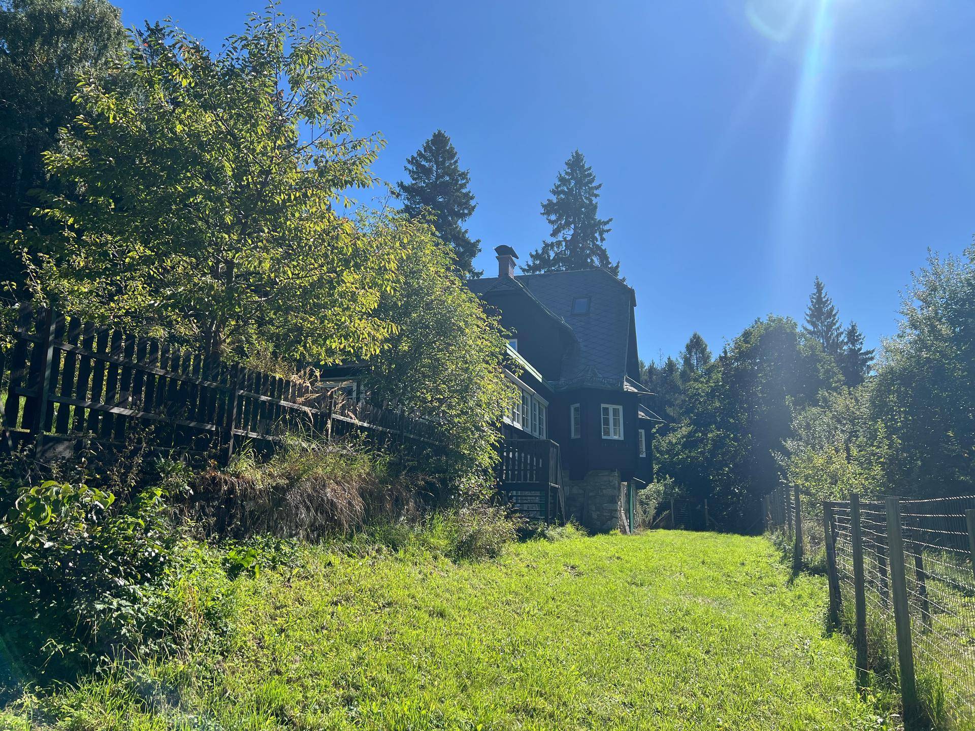 Das Haupthaus von Weitem, umgeben von Bäumen und einem Zaun unter strahlend blauem Himmel.