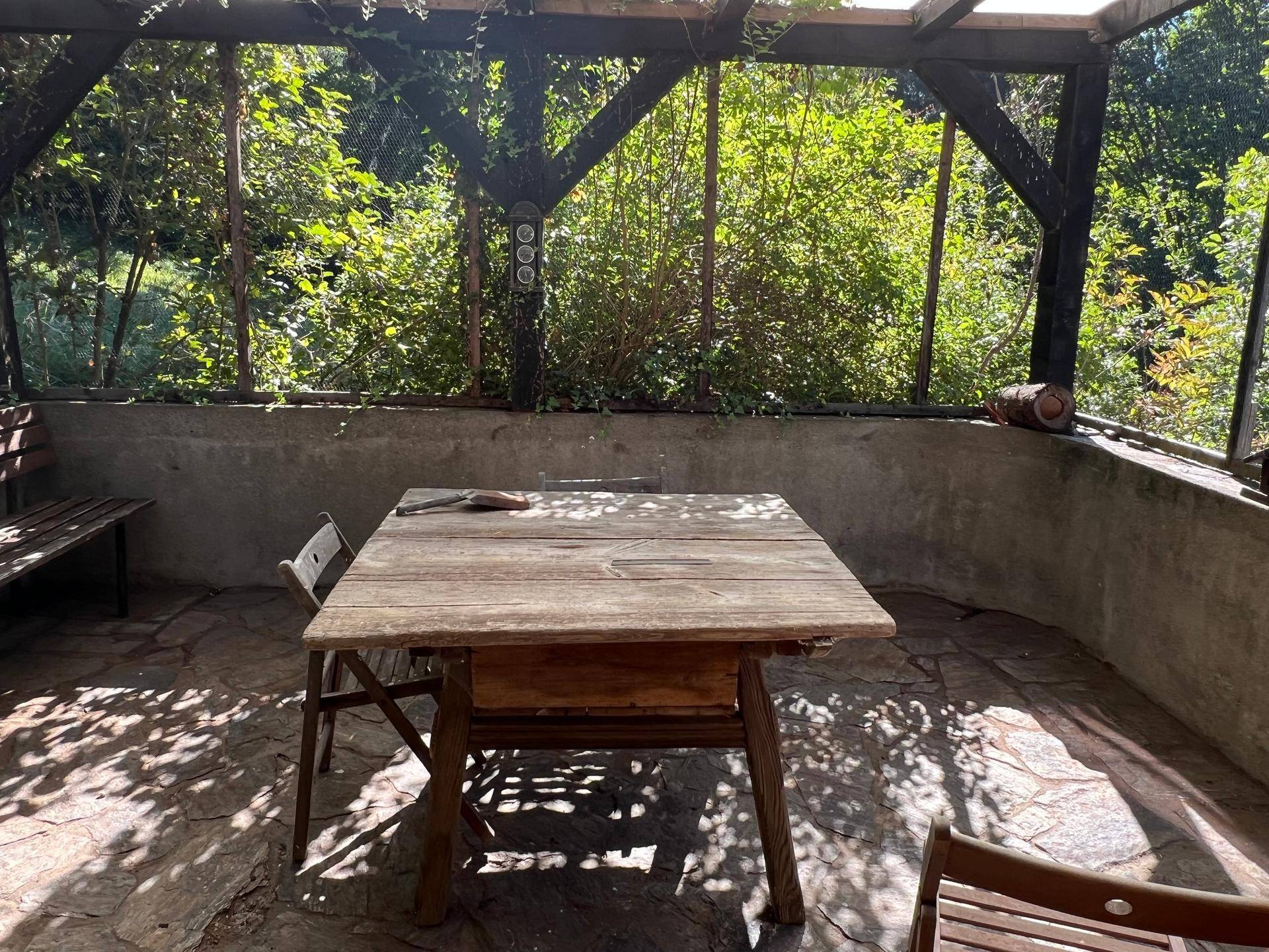 Überdachte Terrasse mit rustikalem Holztisch und Sitzgelegenheiten, umgeben von viel Grün.