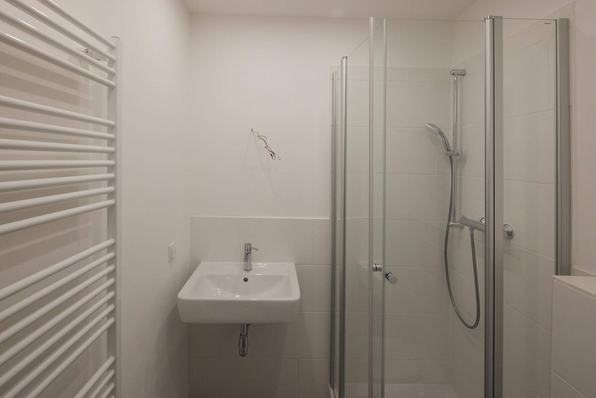 Funktionales Badezimmer mit Duschkabine, Waschbecken und praktischem Handtuchheizkörper.