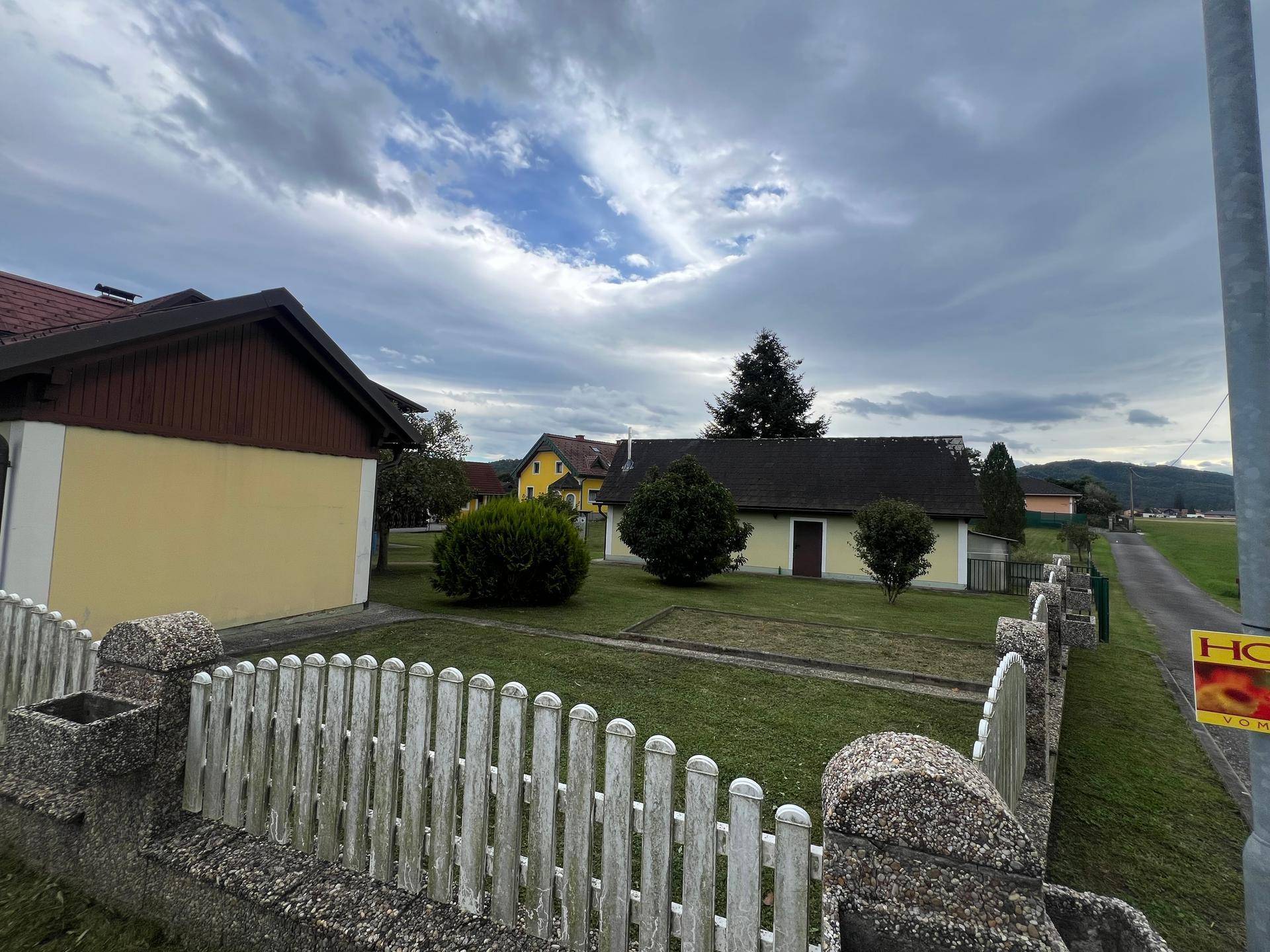 Ansicht des Anwesens von der Straße mit einem Holzzaun und weitem Blick in die Landschaft.