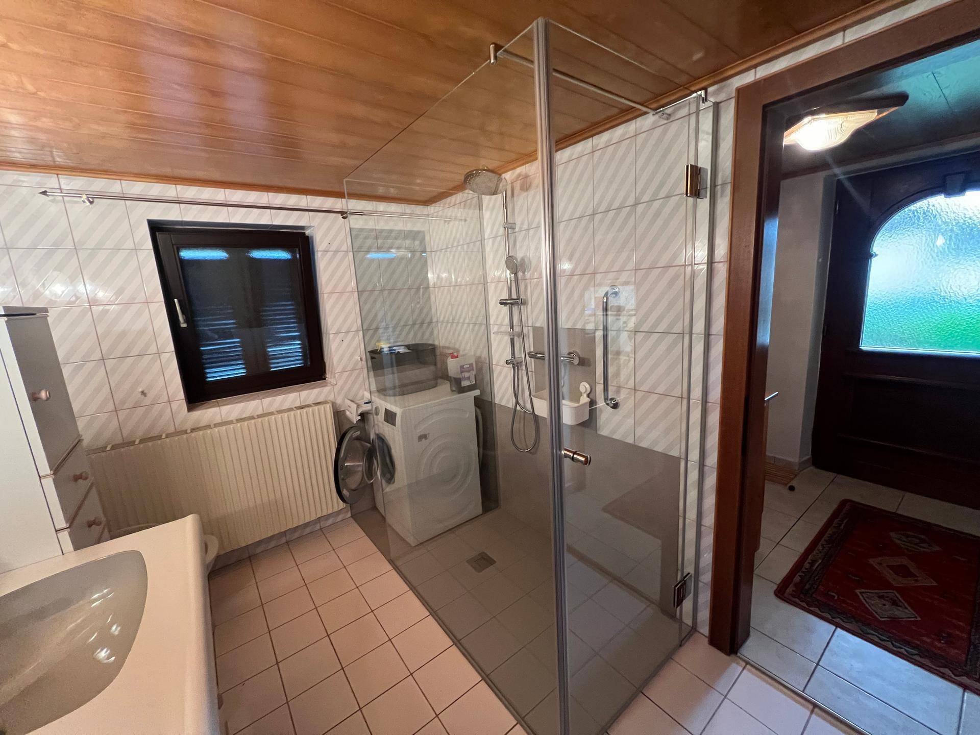 Modernisiertes Badezimmer mit begehbarer Dusche, Waschmaschine und Holzdecke.