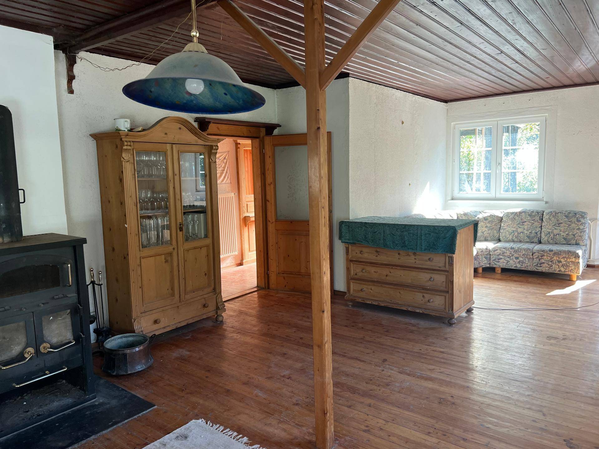Gemütlicher Raum mit Holzdielenboden, sichtbaren Holzbalken und einem traditionellen Holzofen.