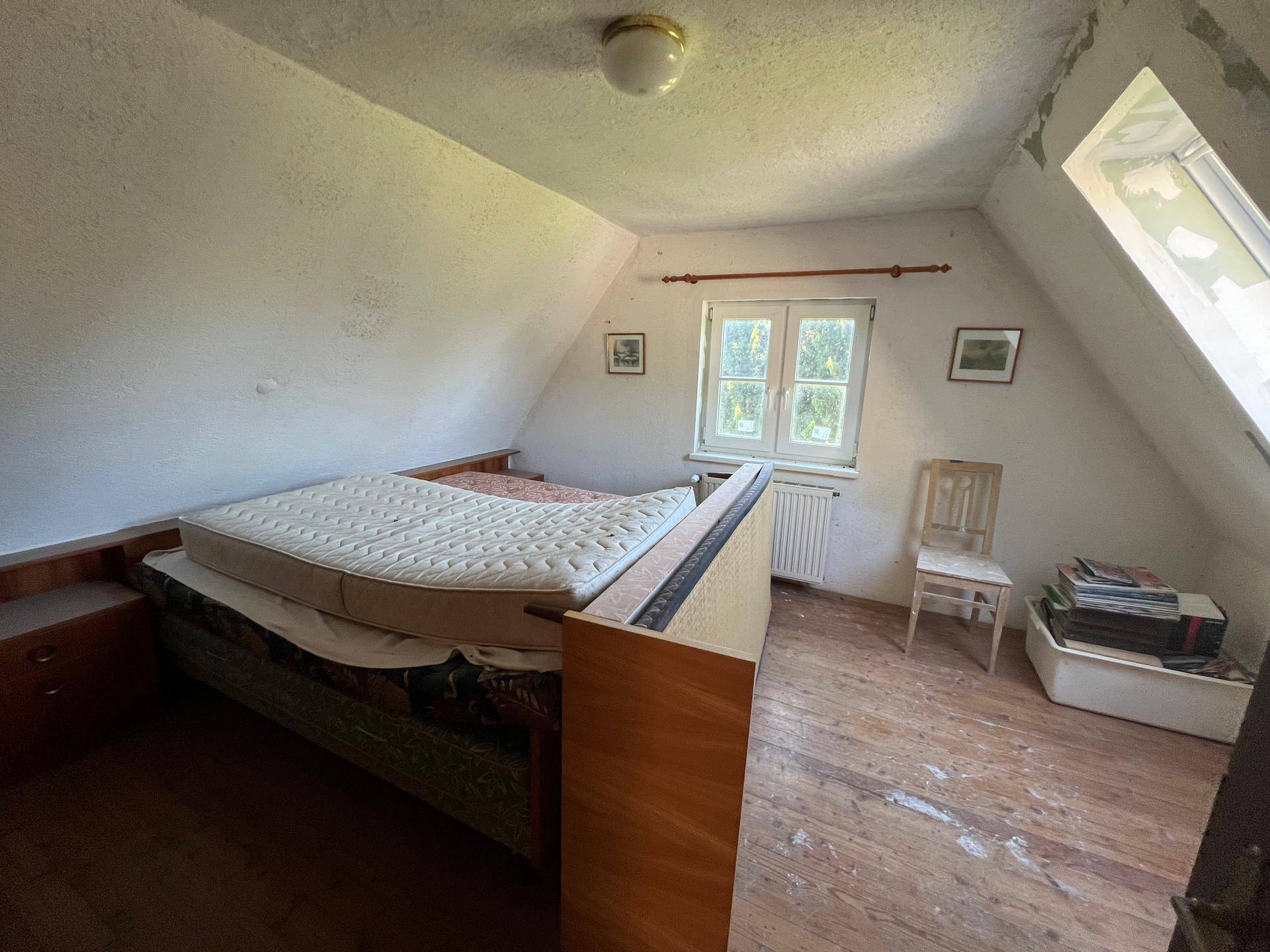 Schlafzimmer im Dachgeschoss mit Holzdielenboden, Bett und schräger Decke.