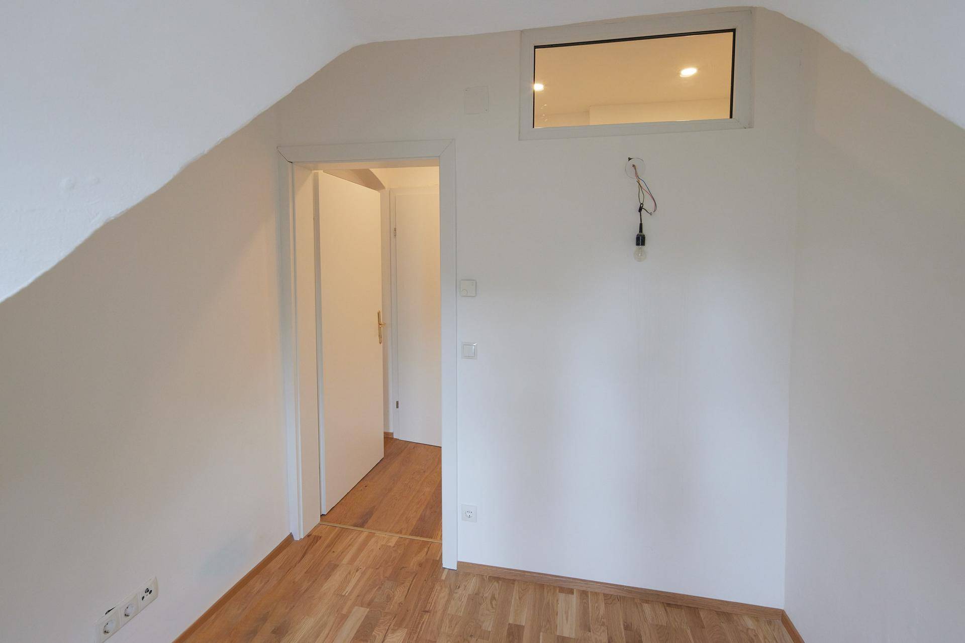 Heller Raum im Dachgeschoss mit Holzboden und Zugang zu einem weiteren Zimmer.