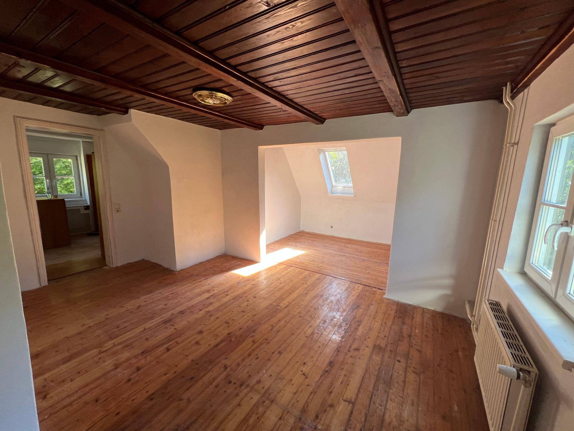 Heller Raum mit Holzdielenboden, sichtbaren Holzbalken und einem Dachfenster für natürliches Licht.
