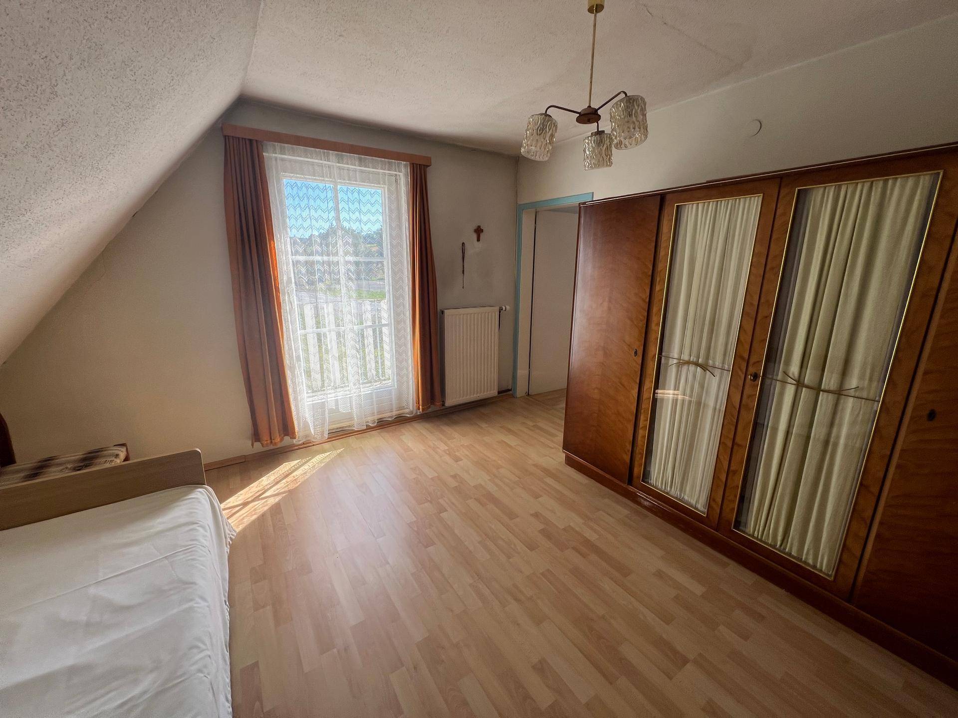 Dachgeschoss-Schlafzimmer mit Laminatboden, großem Kleiderschrank und Fenster.