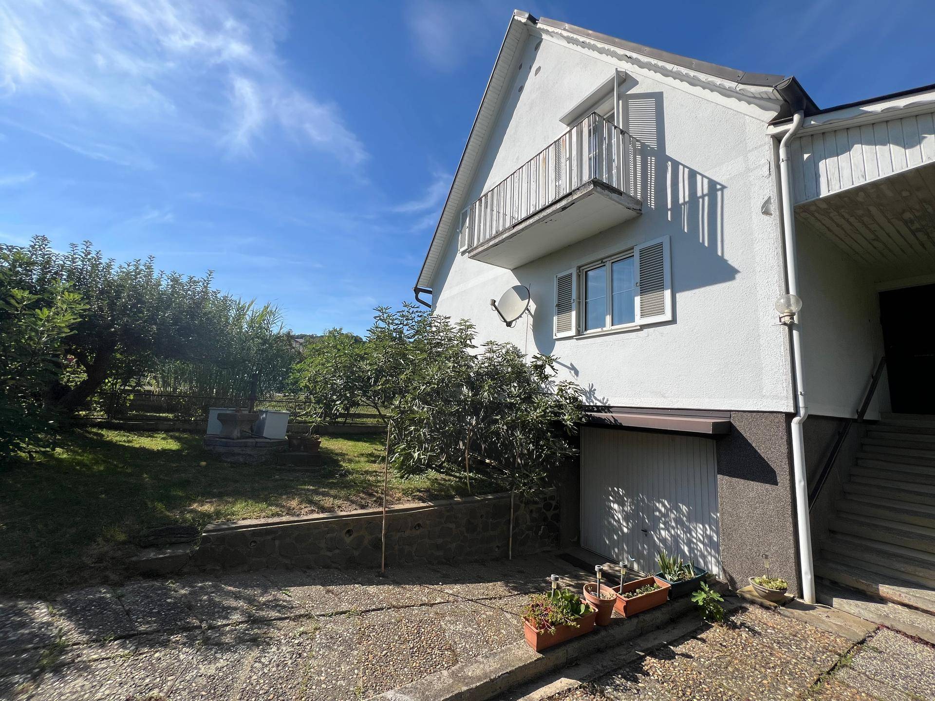 Seitenansicht des Hauses mit Balkon, Einfahrt und angrenzendem Gartenbereich.