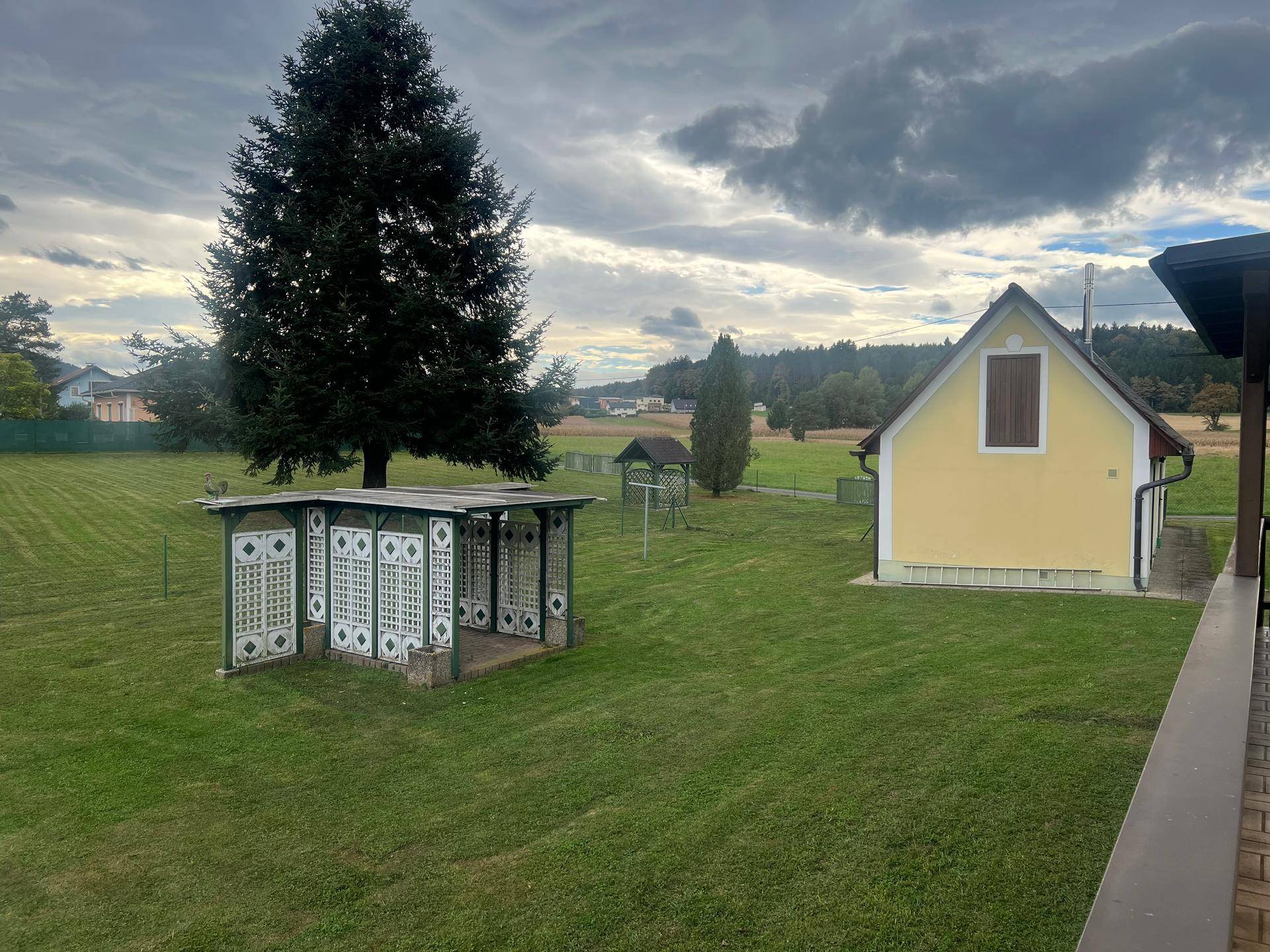 Weitläufiger Garten mit Rasenfläche, hohen Bäumen und einem Pavillon im Hintergrund.