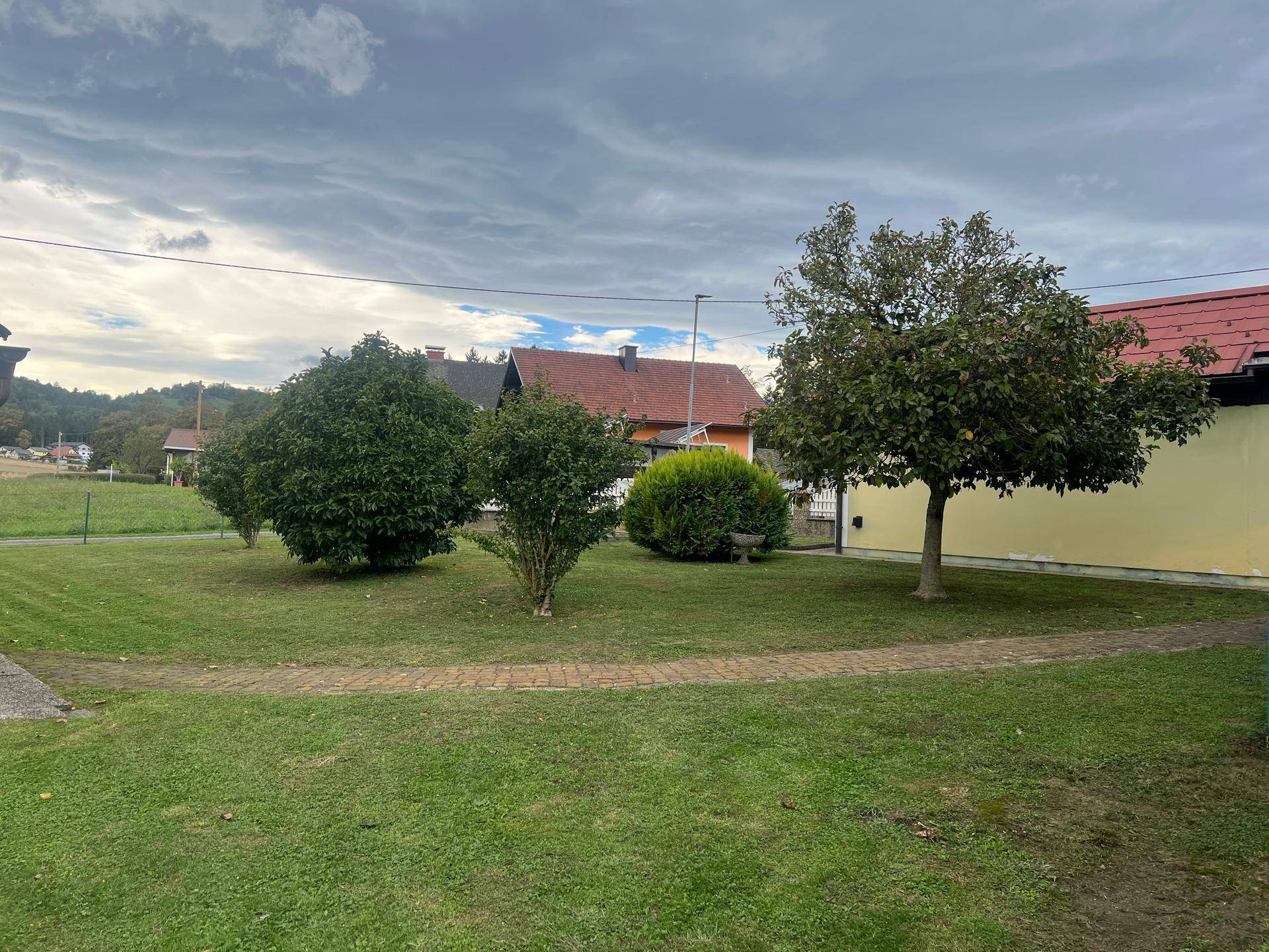 Gepflegter Gartenbereich mit verschiedenen Bäumen und Sträuchern, umgeben von Rasen.