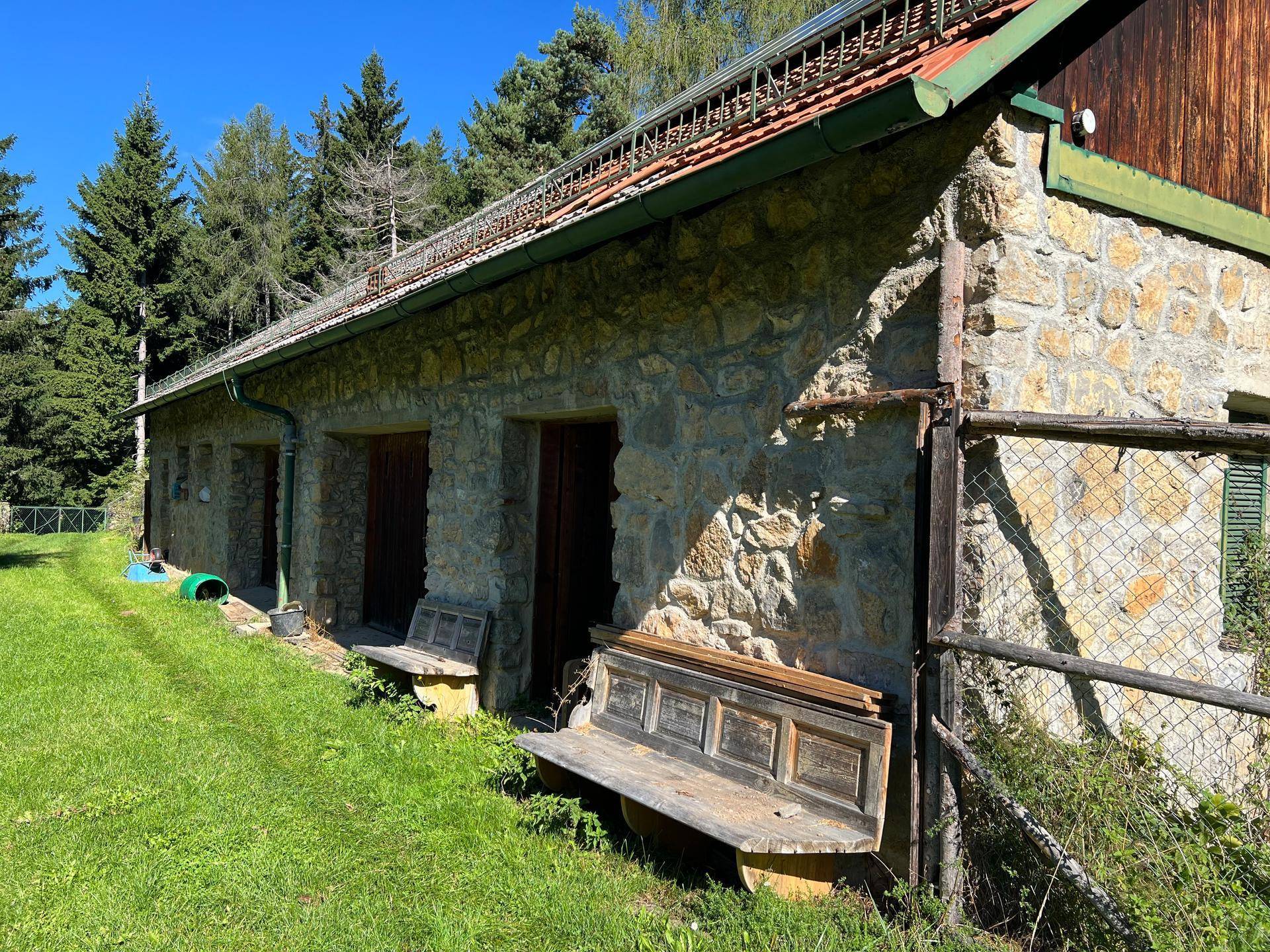 Steinfassade eines Nebengebäudes mit Holzbänken und einer grünen Wiese im Vordergrund.