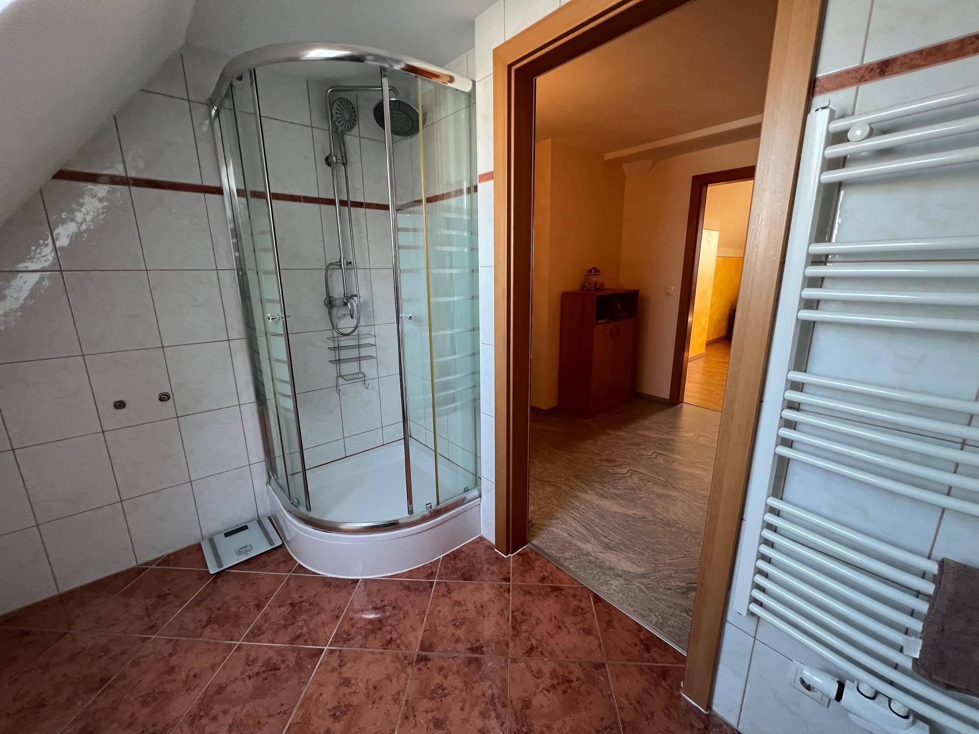 Badezimmer mit Eckduschkabine, gefliestem Boden und beheiztem Handtuchhalter.