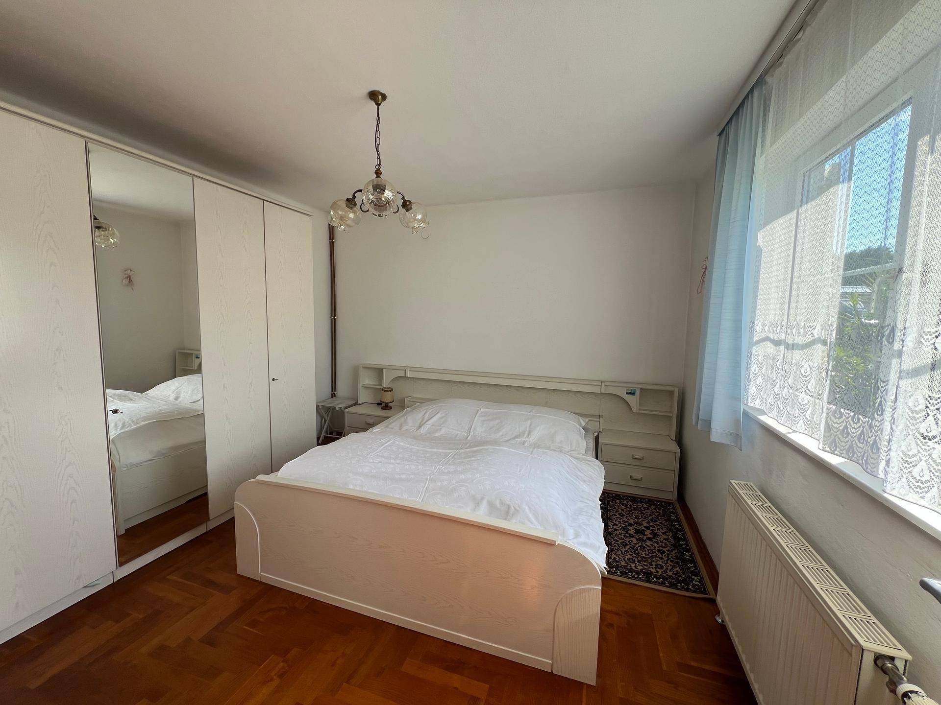 Schlafzimmer mit Doppelbett, Spiegelschrank und Parkettboden, hell beleuchtet.