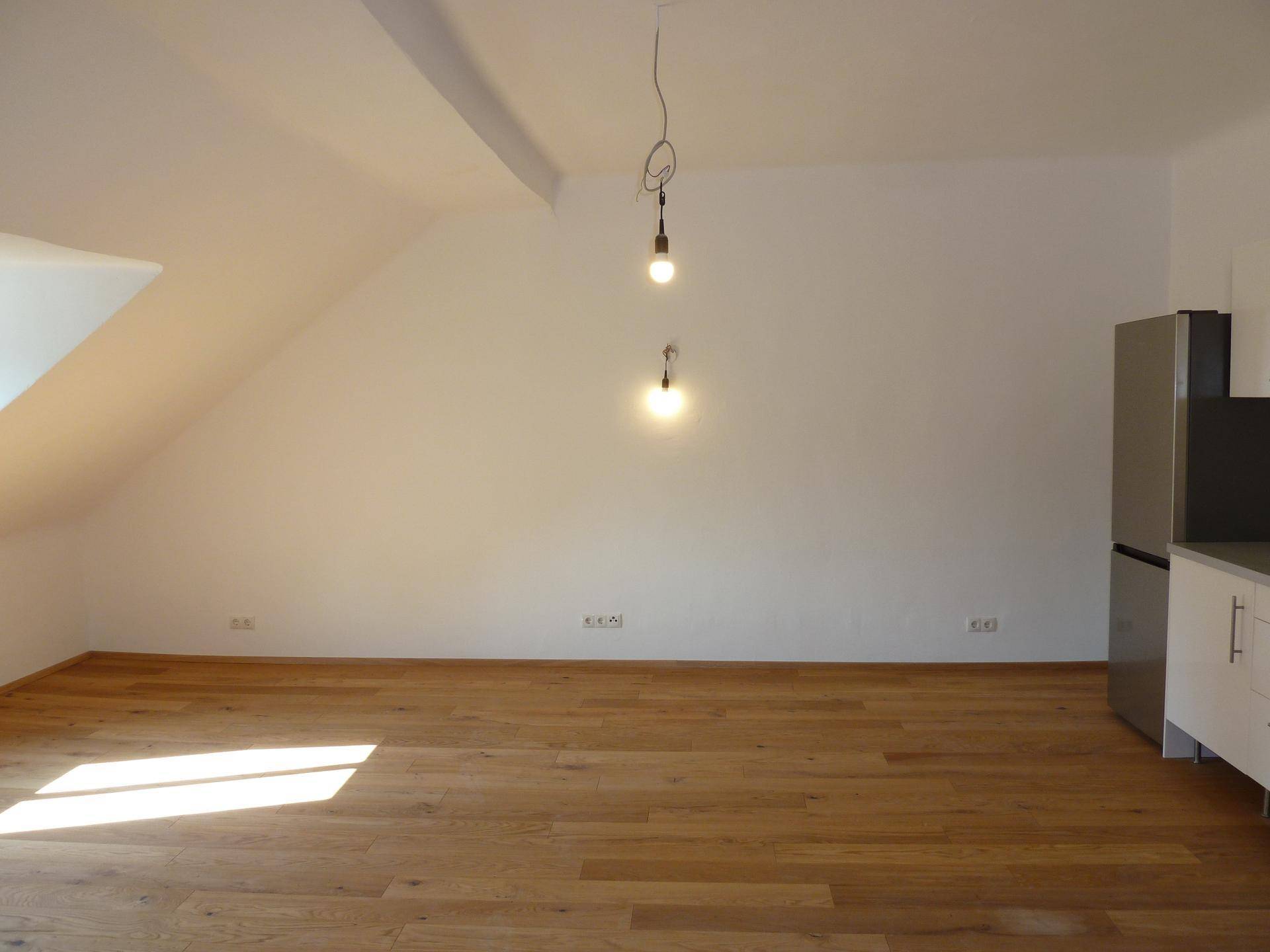 Offener Wohnbereich mit Holzboden und Dachschrägen, teilweise mit Küchenzeile.