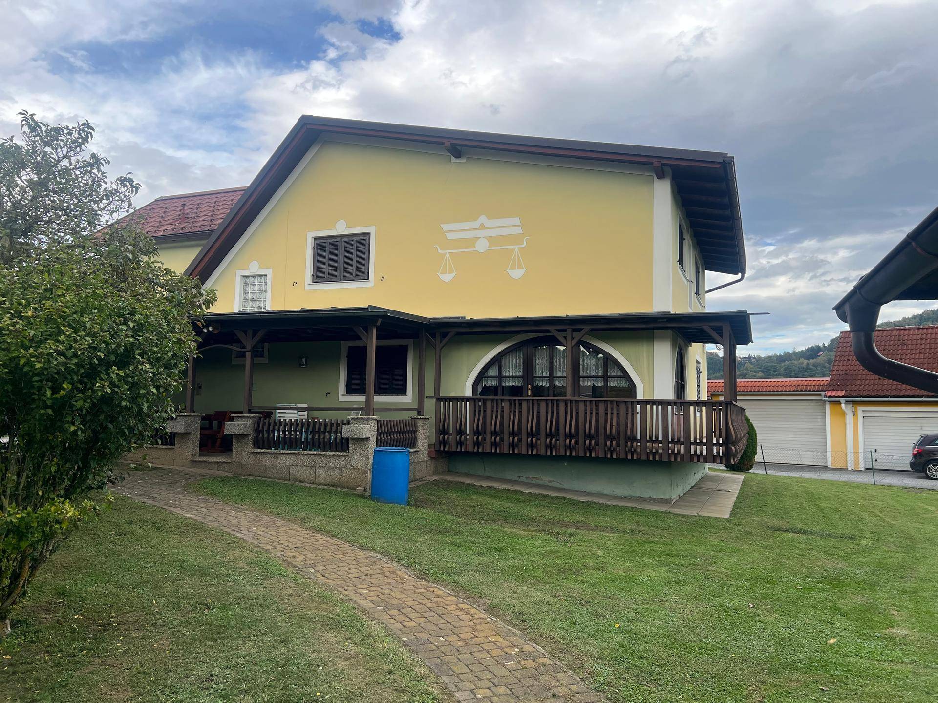Überdachte Terrasse mit Holzbalkon und Zugang zum gepflegten Gartenbereich des Hauses.