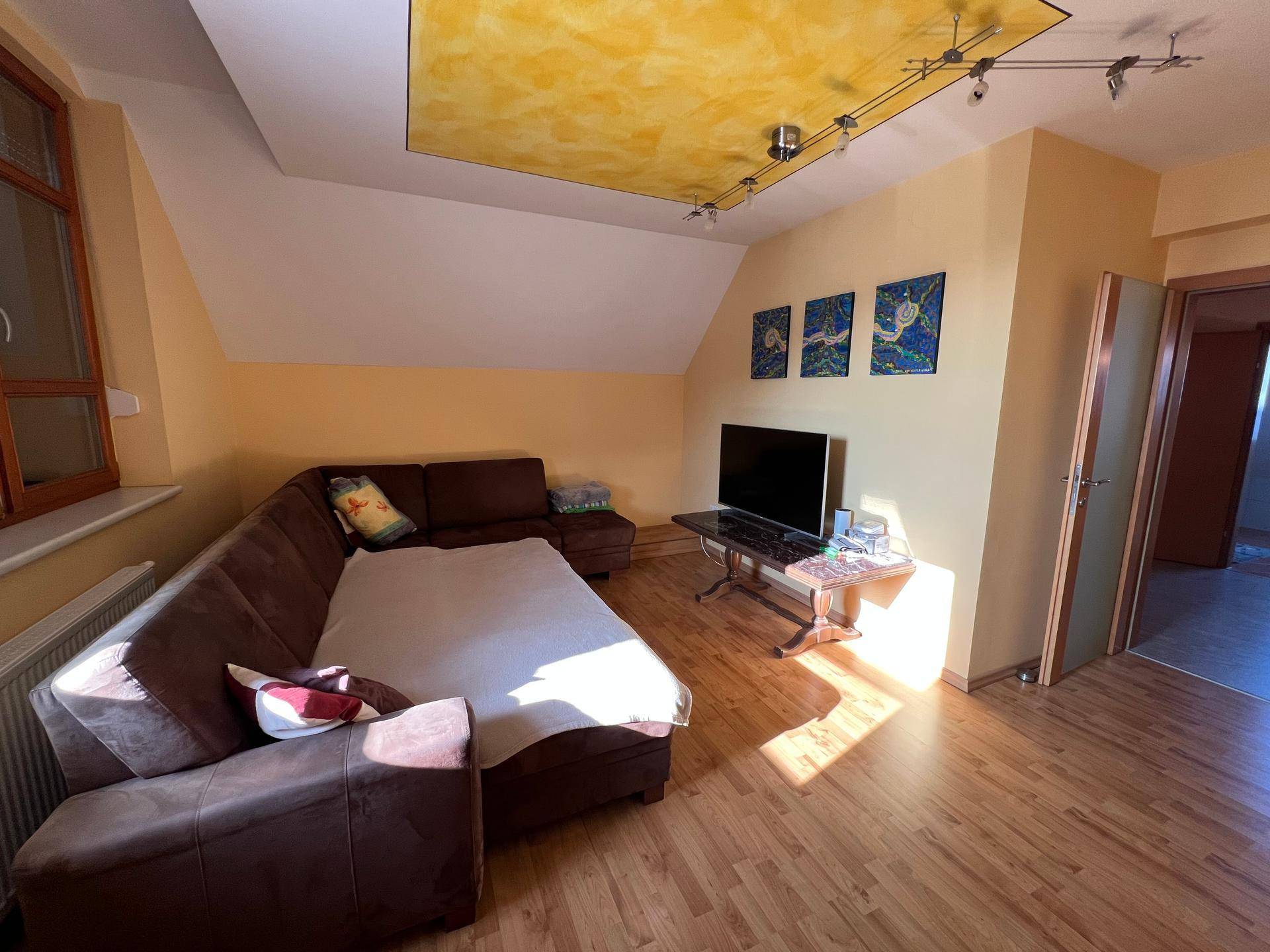Gemütliches Wohnzimmer mit Ecksofa, Fernseher und Dachschräge, ausgestattet mit Holzboden.
