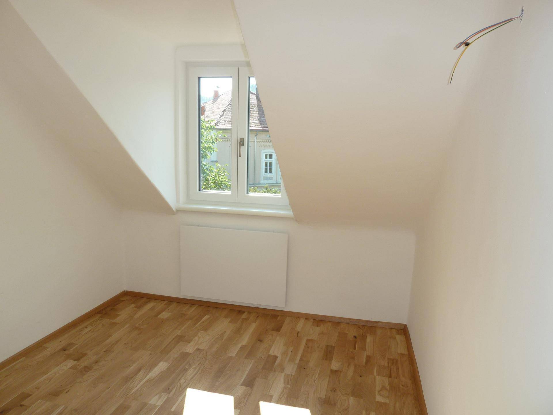 Gemütlicher Raum im Dachgeschoss mit Holzboden, schrägen Wänden und Ausblick ins Grüne.