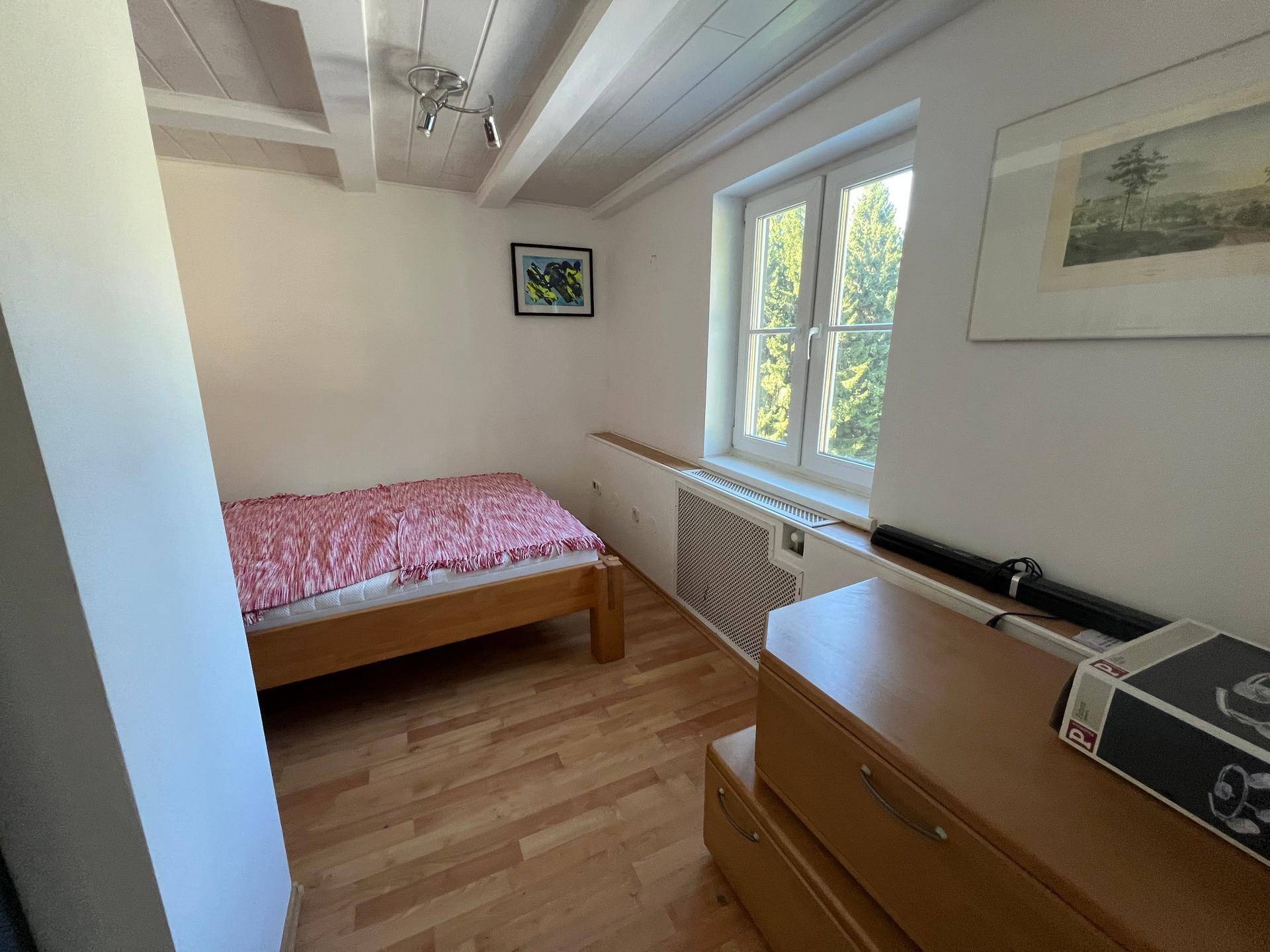 Kleines Schlafzimmer mit Laminatboden und Fenster mit Blick ins Grüne.