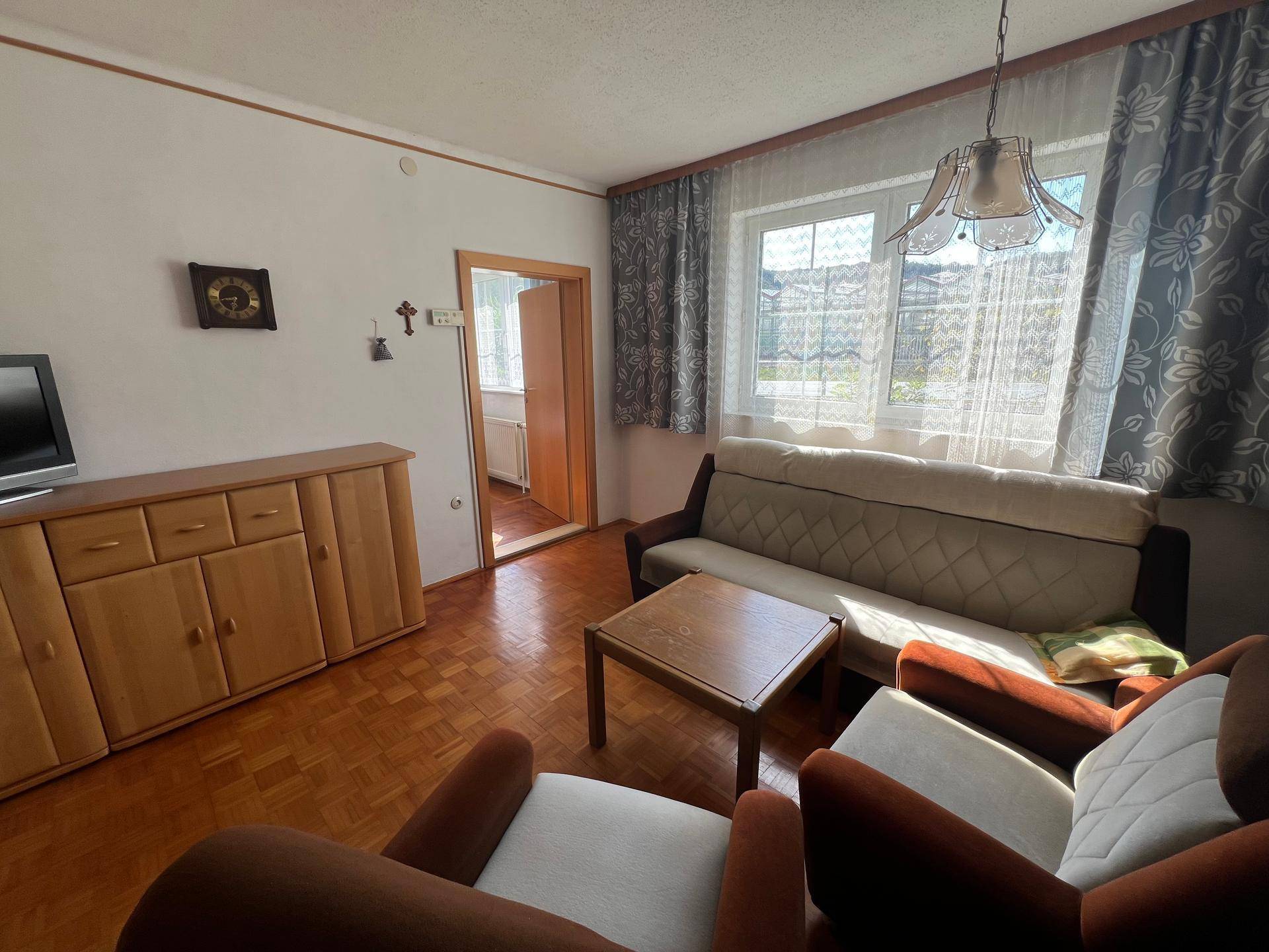 Wohnzimmer mit Parkettboden, bequemen Sitzmöbeln und Fenster mit Vorhängen.