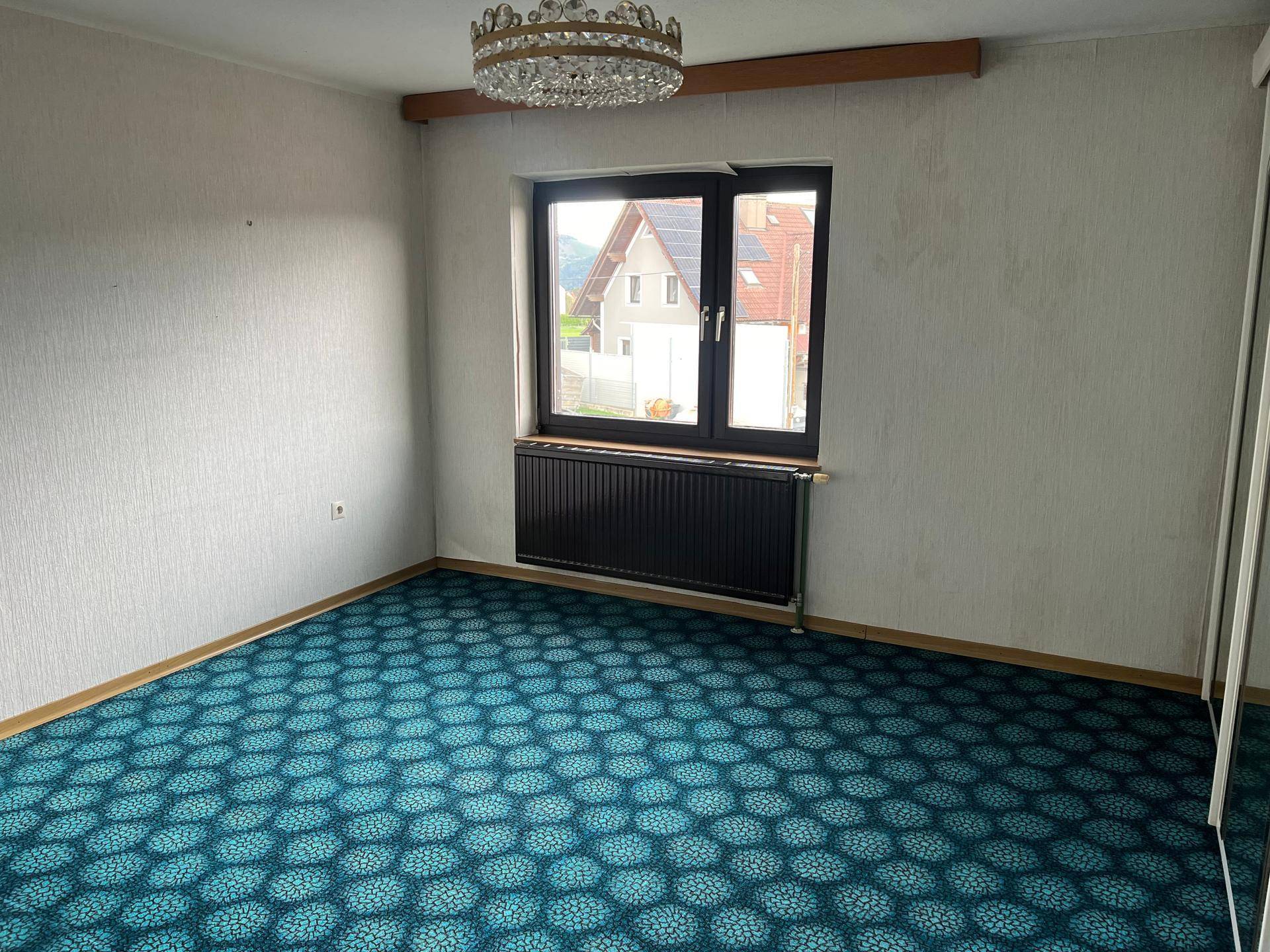 Schlafzimmer mit auffälligem blauem Teppichboden, Fenster und einem Kronleuchter an der Decke.
