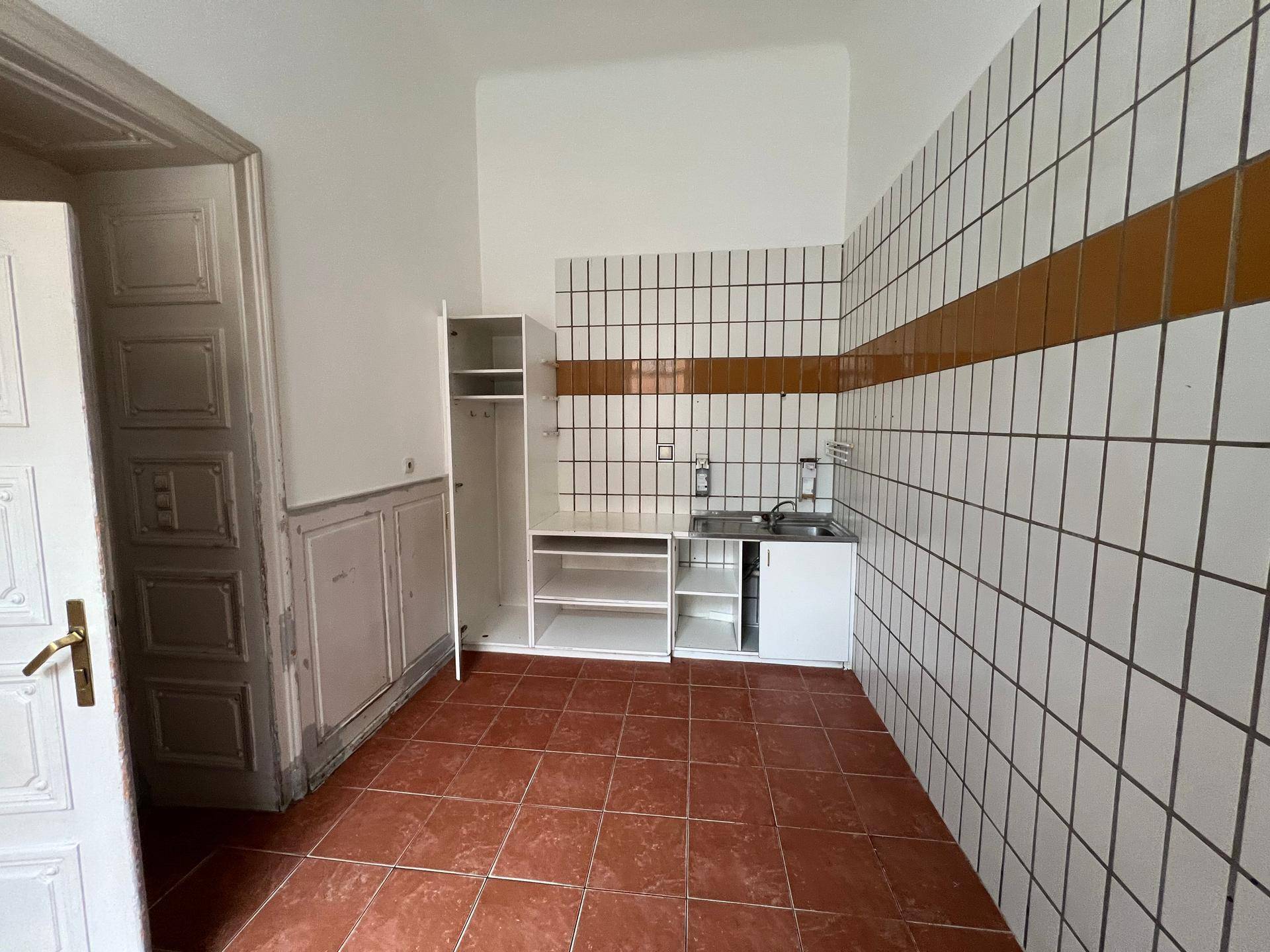 Einfacher Küchenbereich mit gefliesten Wänden, Spülbecken und grundlegenden Schränken.