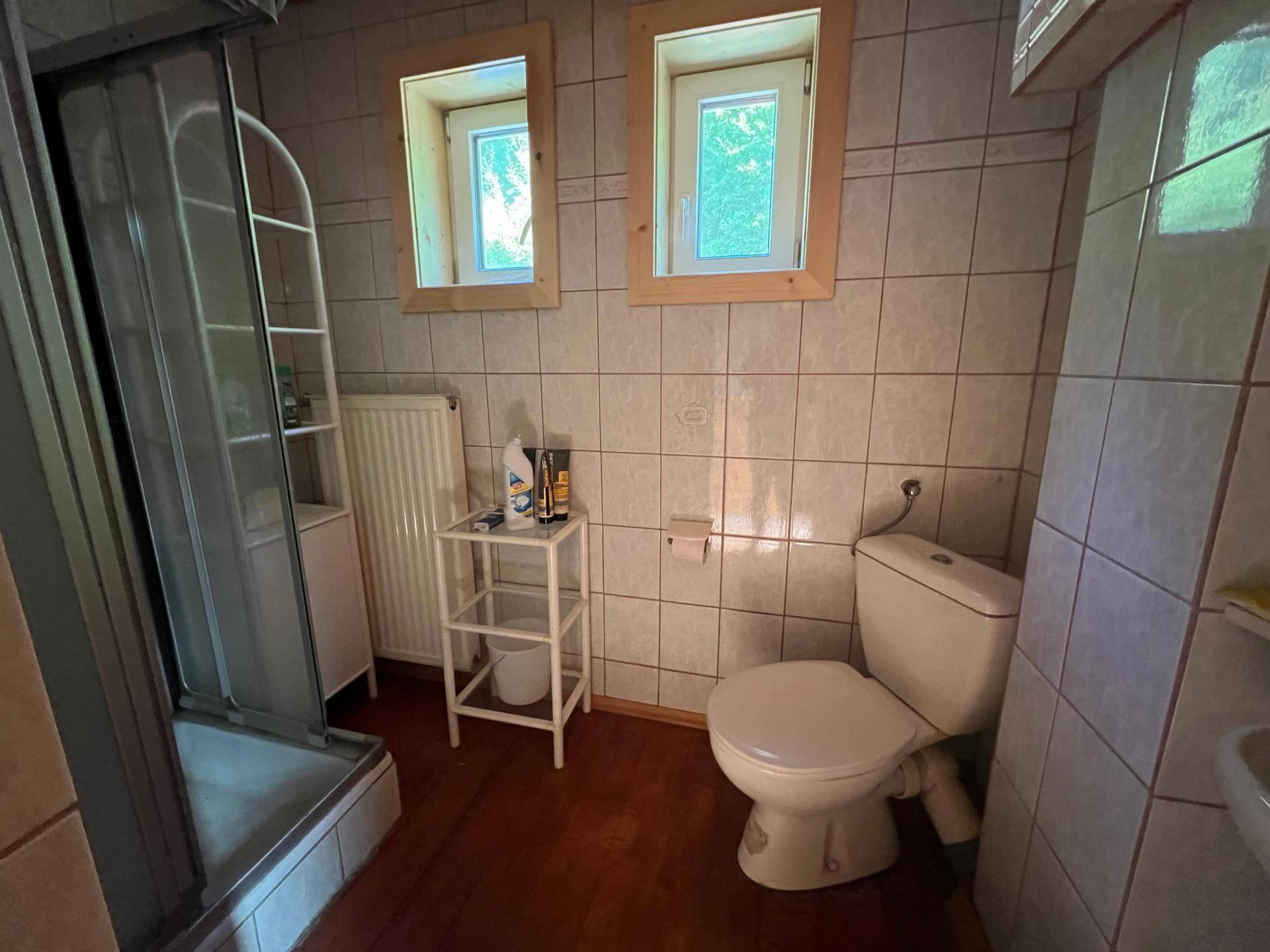 Badezimmer mit gefliesten Wänden, Duschkabine, WC und zwei Fenstern.