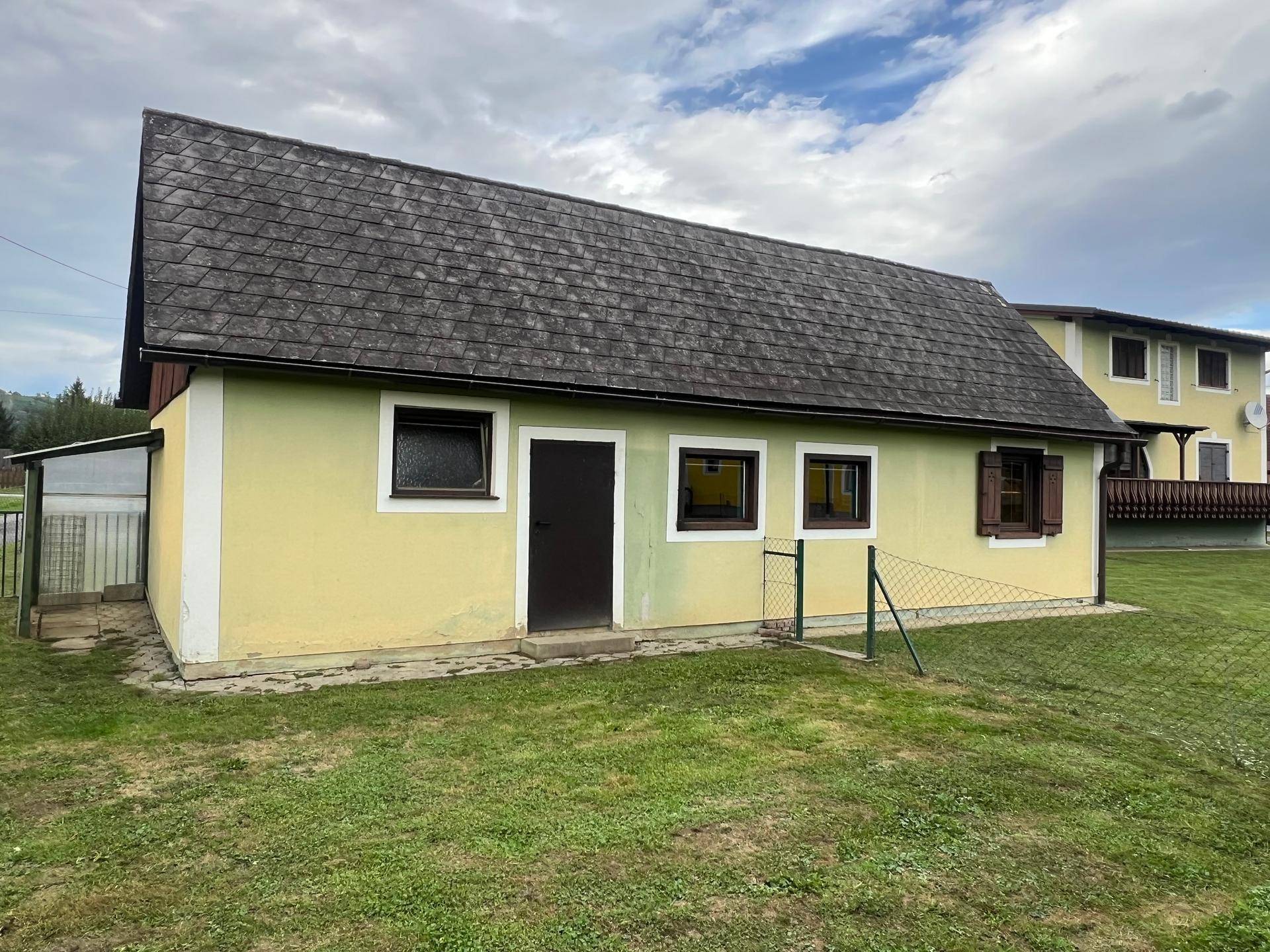 Kleines Nebengebäude im Gartenbereich mit einfacher Fassade und Fenstern.