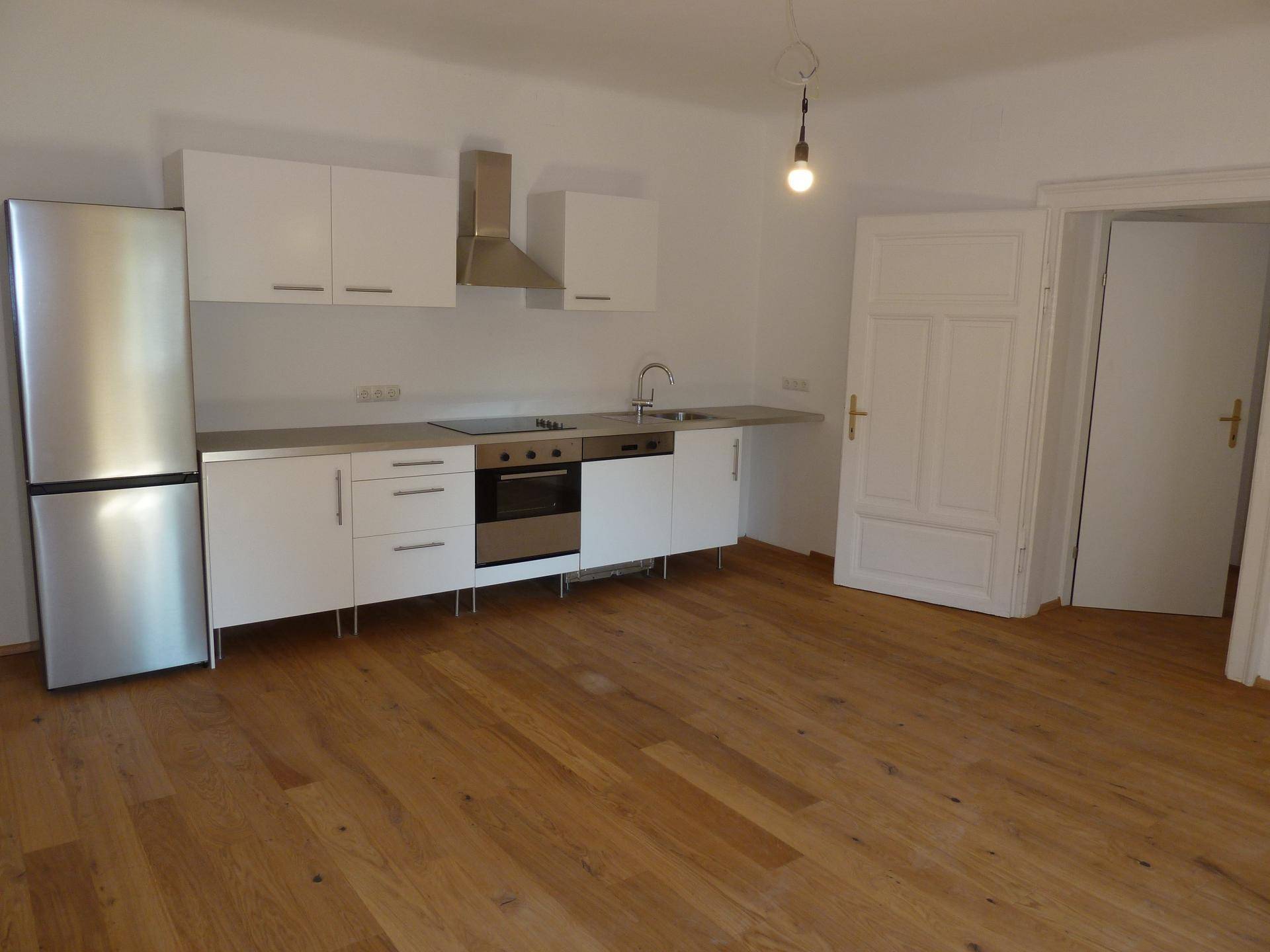 Funktionale Einbauküche mit weißen Fronten und Holzboden, angrenzend an einen weiteren Raum.
