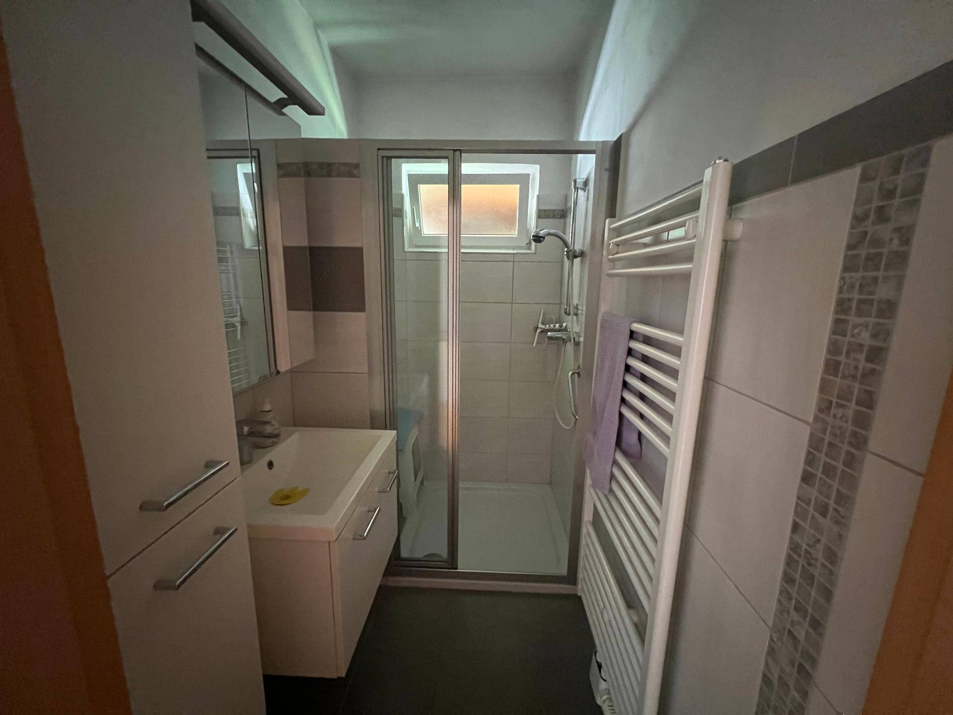Modernisiertes Badezimmer mit Duschkabine, Waschtisch und beheiztem Handtuchhalter.