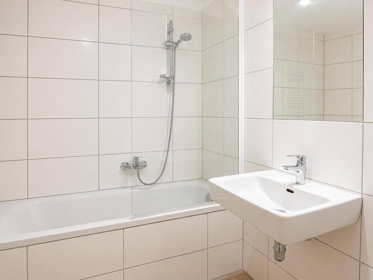 Modernes Badezimmer mit weißen Fliesen, Badewanne mit Duschfunktion und einem einzelnen Waschbecken.