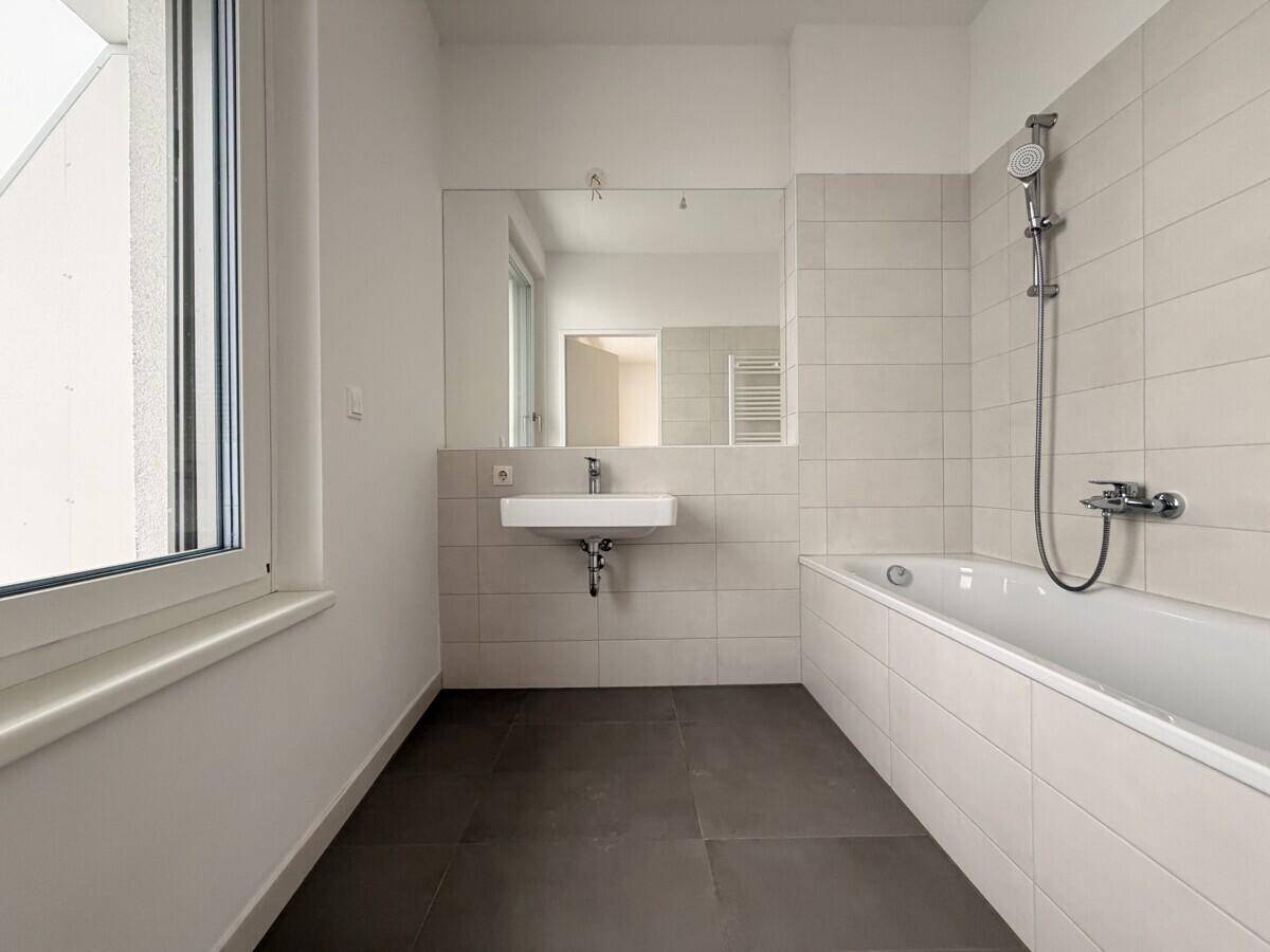 Modernes Badezimmer mit Badewanne, Einzelwaschbecken und großem Fenster für Tageslicht.