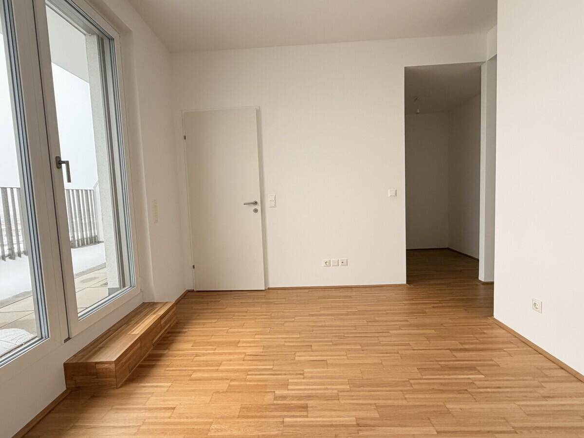 Heller Flur mit Parkettboden und weiß gestrichenen Wänden, der zu weiteren Räumen führt.