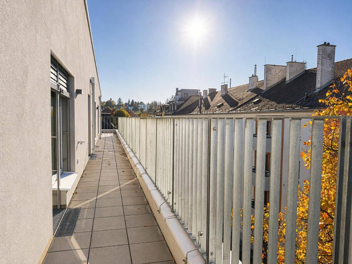 Langer, sonniger Balkon mit Metallgeländer und Blick über die Dächer der Stadt.