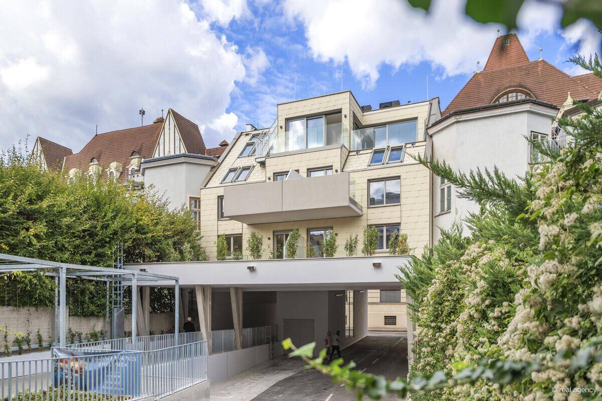 Moderne Gebäudefassade mit Balkonen und Zufahrt zur Tiefgarage, umgeben von Grünflächen.