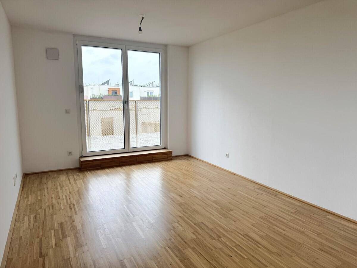 Heller, leerer Raum mit Parkettboden und großer Fensterfront, ideal für ein Wohnzimmer.
