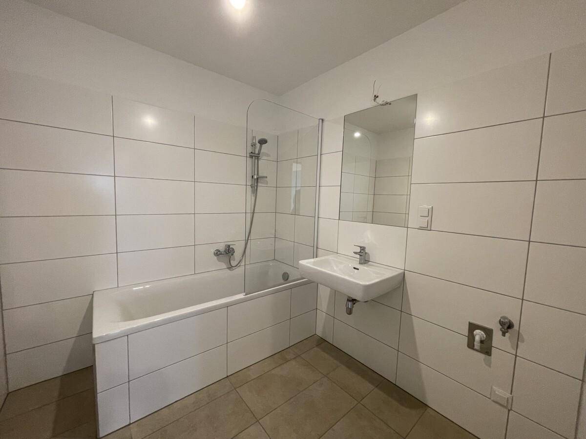 Modernes Badezimmer mit weißen Fliesen, Badewanne mit Duschfunktion und Einzelwaschbecken.
