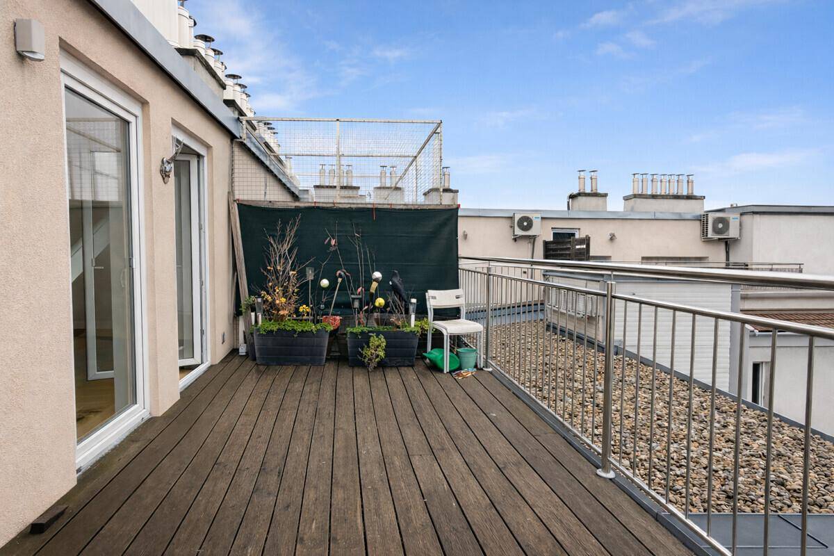 Dachterrasse mit Holzboden, Pflanzen und Blick auf die umliegenden Gebäude.