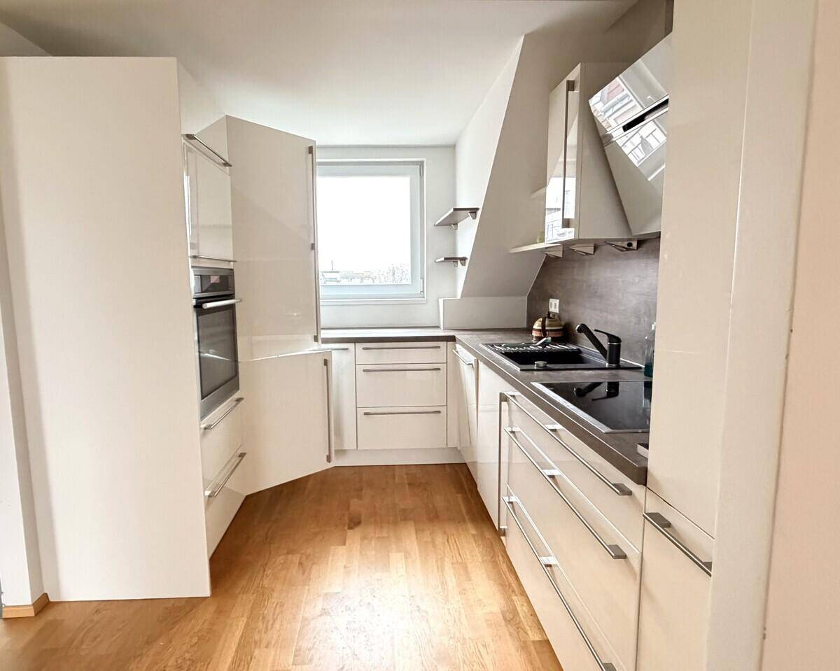 Moderne Einbauküche mit weißen Hochglanzfronten, Induktionskochfeld und Holzboden.