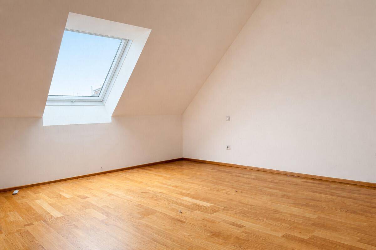 Leerer Raum im Dachgeschoss mit Holzboden und einem einzelnen Dachfenster.