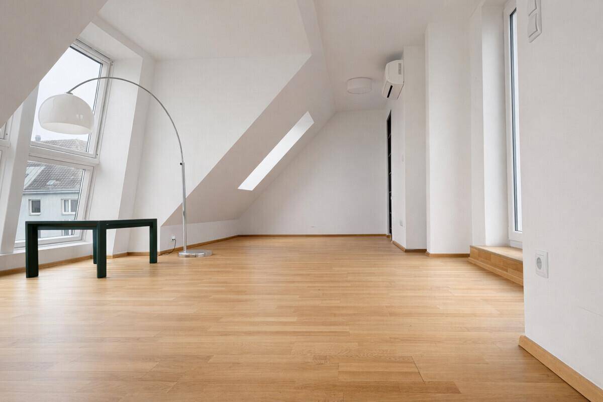 Heller, leerer Raum im Dachgeschoss mit großen Fenstern und Holzboden.