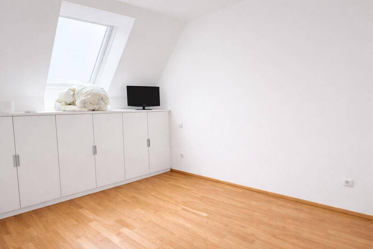 Heller Raum mit Dachfenster, integrierten Schränken und Holzboden.