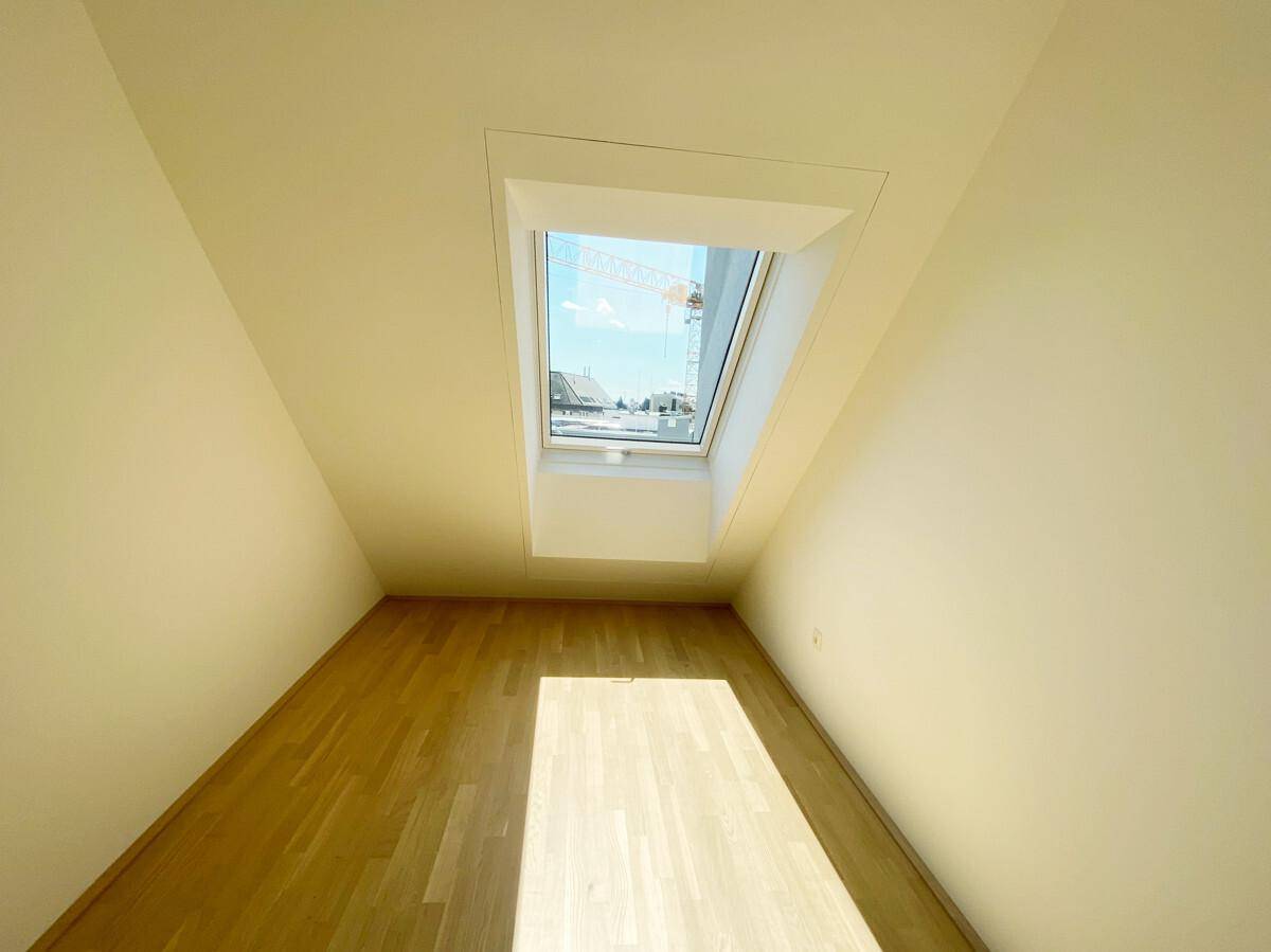 Gemütliches Zimmer mit Holzboden und einem Dachfenster, das viel natürliches Licht hereinlässt.