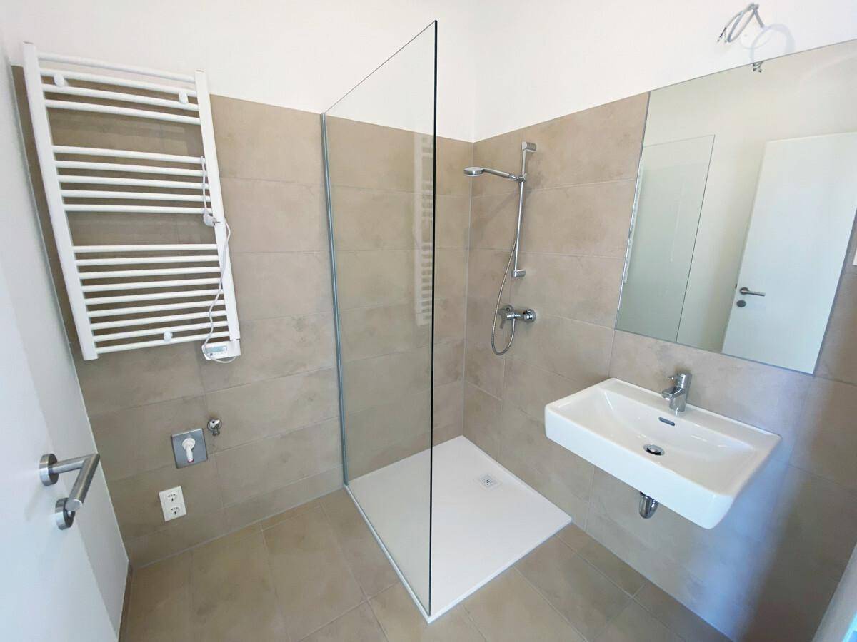Modernes Badezimmer mit beigen Fliesen, einer begehbaren Dusche und einem beheizten Handtuchhalter.