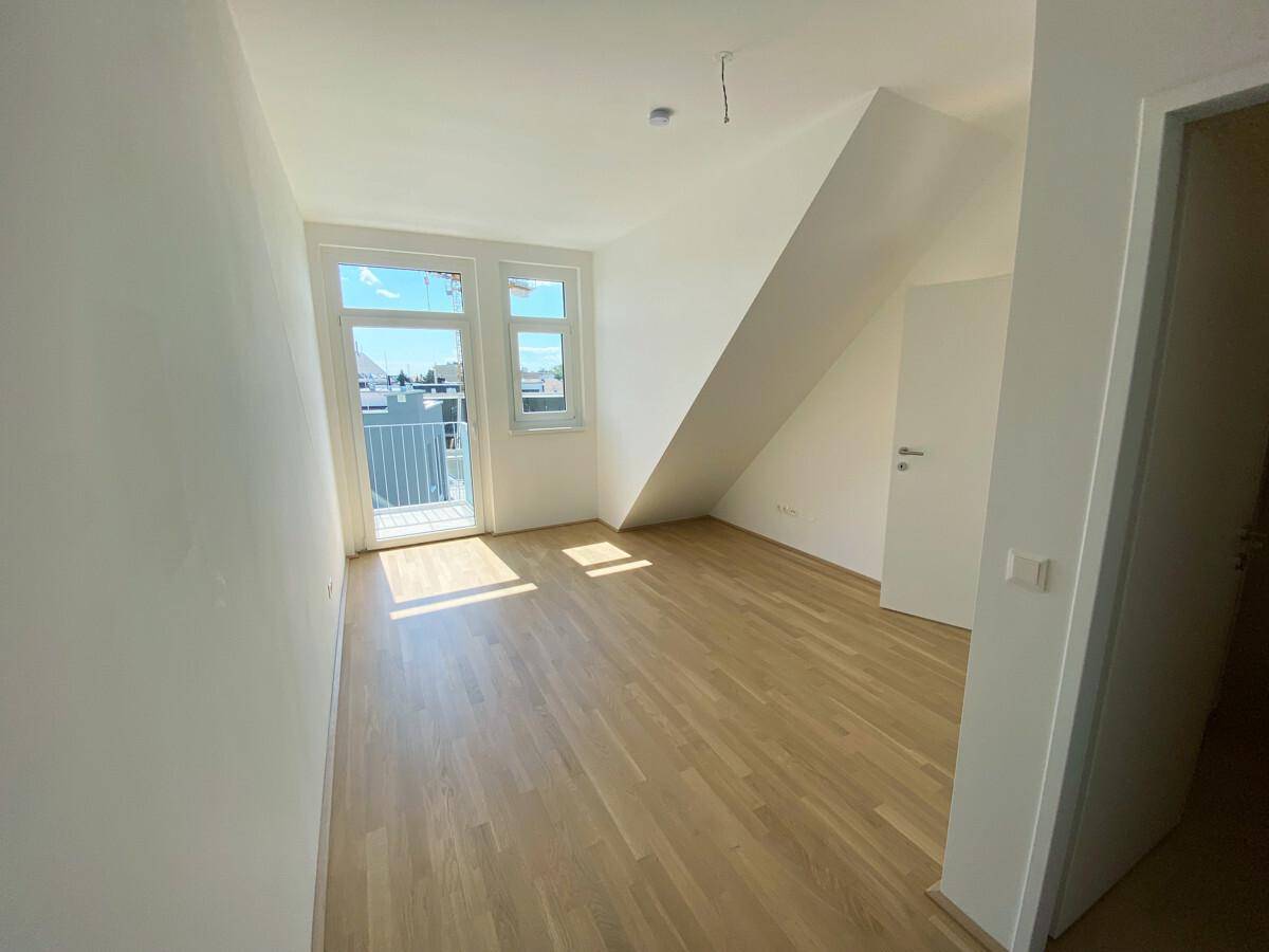 Helles Zimmer mit Holzboden, schräger Decke und Zugang zu einem kleinen Balkon, ideal als Schlafzimmer.