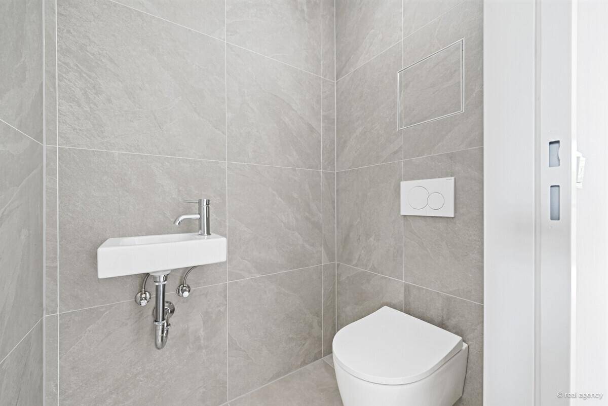 Zeitgemäßes Gäste-WC mit grauen Fliesen, wandhängendem WC und kleinem Handwaschbecken.