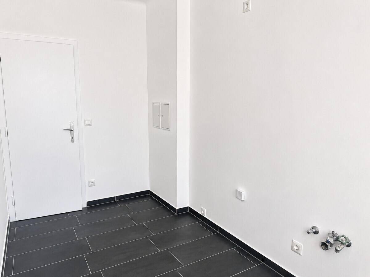 Praktischer Raum mit dunklem Fliesenboden und Anschlüssen, ideal als Hauswirtschaftsraum.