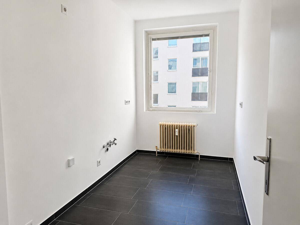 Funktionaler Raum mit dunklen Fliesen, Fenster und Anschlüssen für Waschmaschine oder Küche.